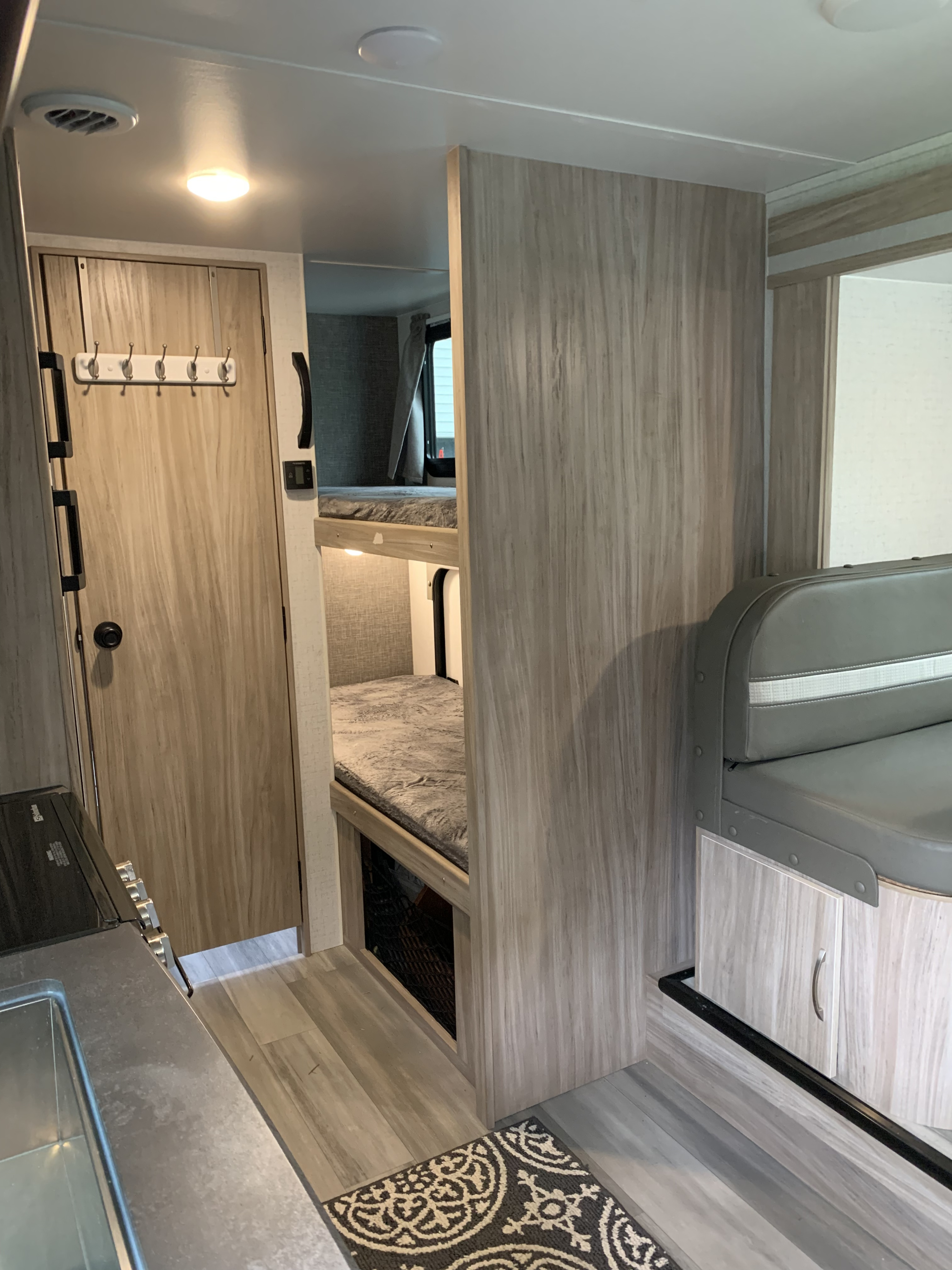 RV rental interior showcasing compact living with bunk beds, a small kitchen, and a dining booth. Light wood accents provide a modern feel.. Winnebago Micro Minnie 2021