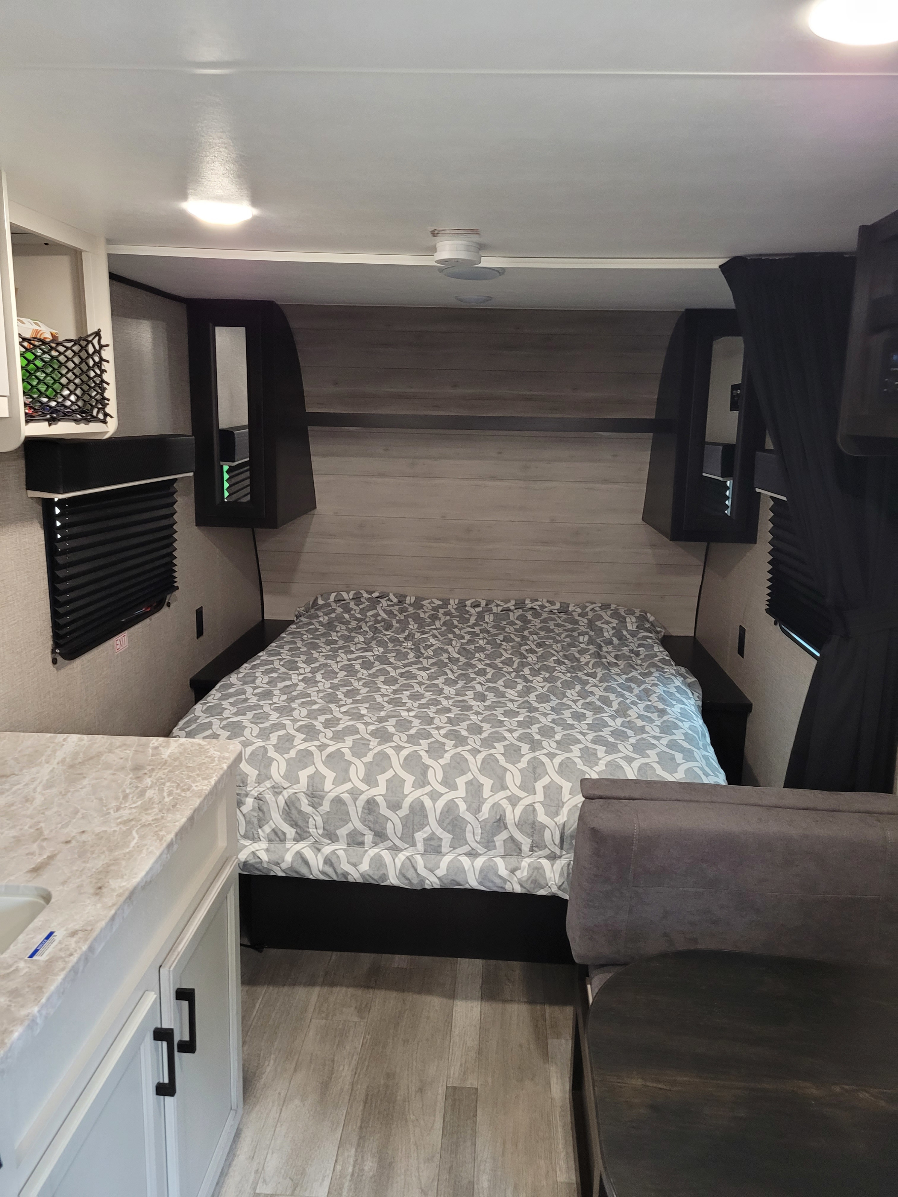 Cozy RV rental interior featuring a patterned bed, overhead cabinets, and a partial view of the compact kitchen and dining area.. Jayco Jay Flight SLX 2022