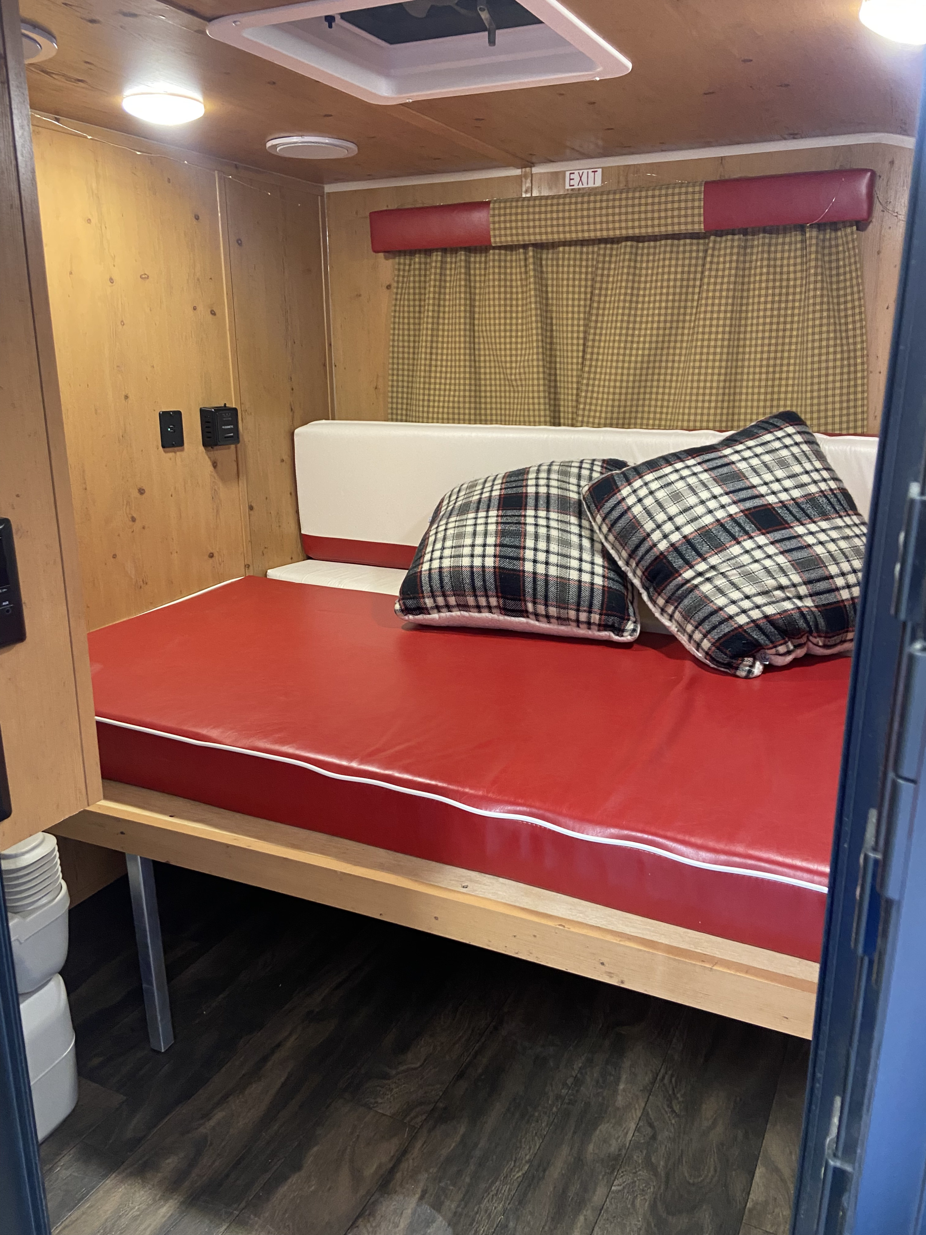Cozy RV rental interior features a red mattress with plaid pillows, wood paneling, and an overhead vent, creating a functional sleeping area.. Sunset Park RV SunRay 2020