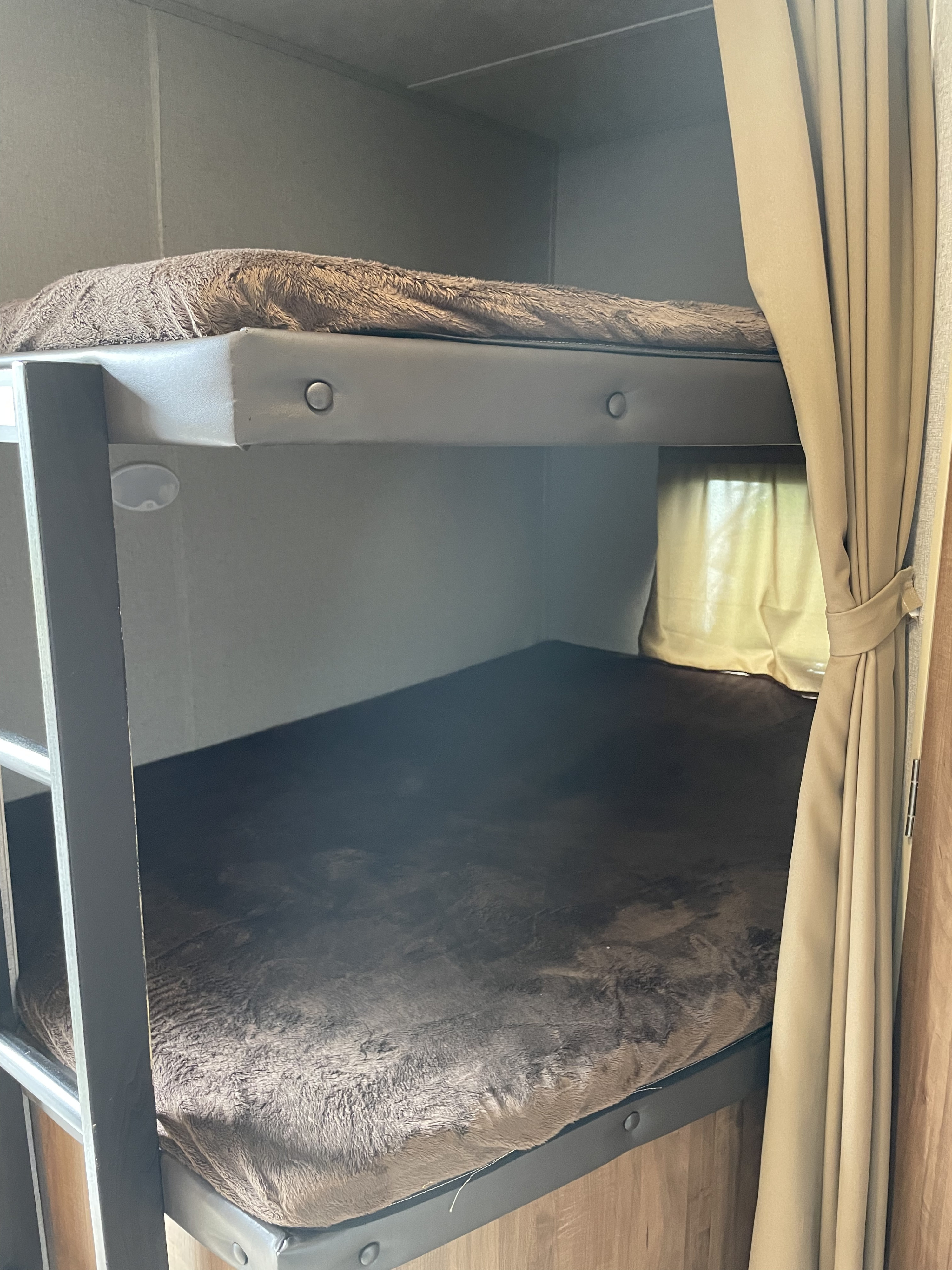 Inside an RV rental, showing neat bunk beds with fluffy brown covers and a small window for natural light.. Dutchmen Aspen Trail 2790BHS 2019