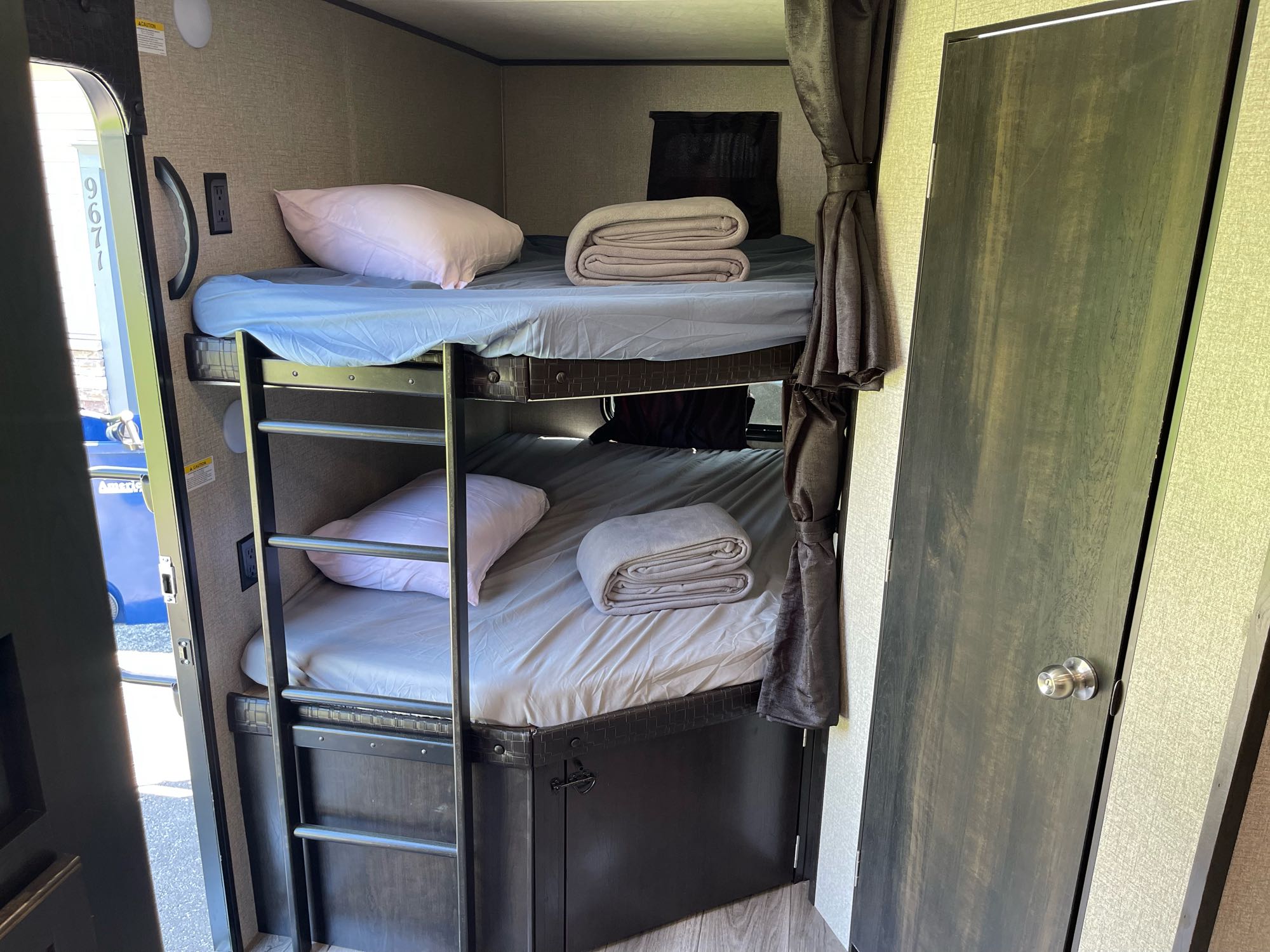 RV rental interior showing bunk beds with bedding, a ladder, and an electrical outlet. A dark door is on the right.. Jayco Jay Flight 2021