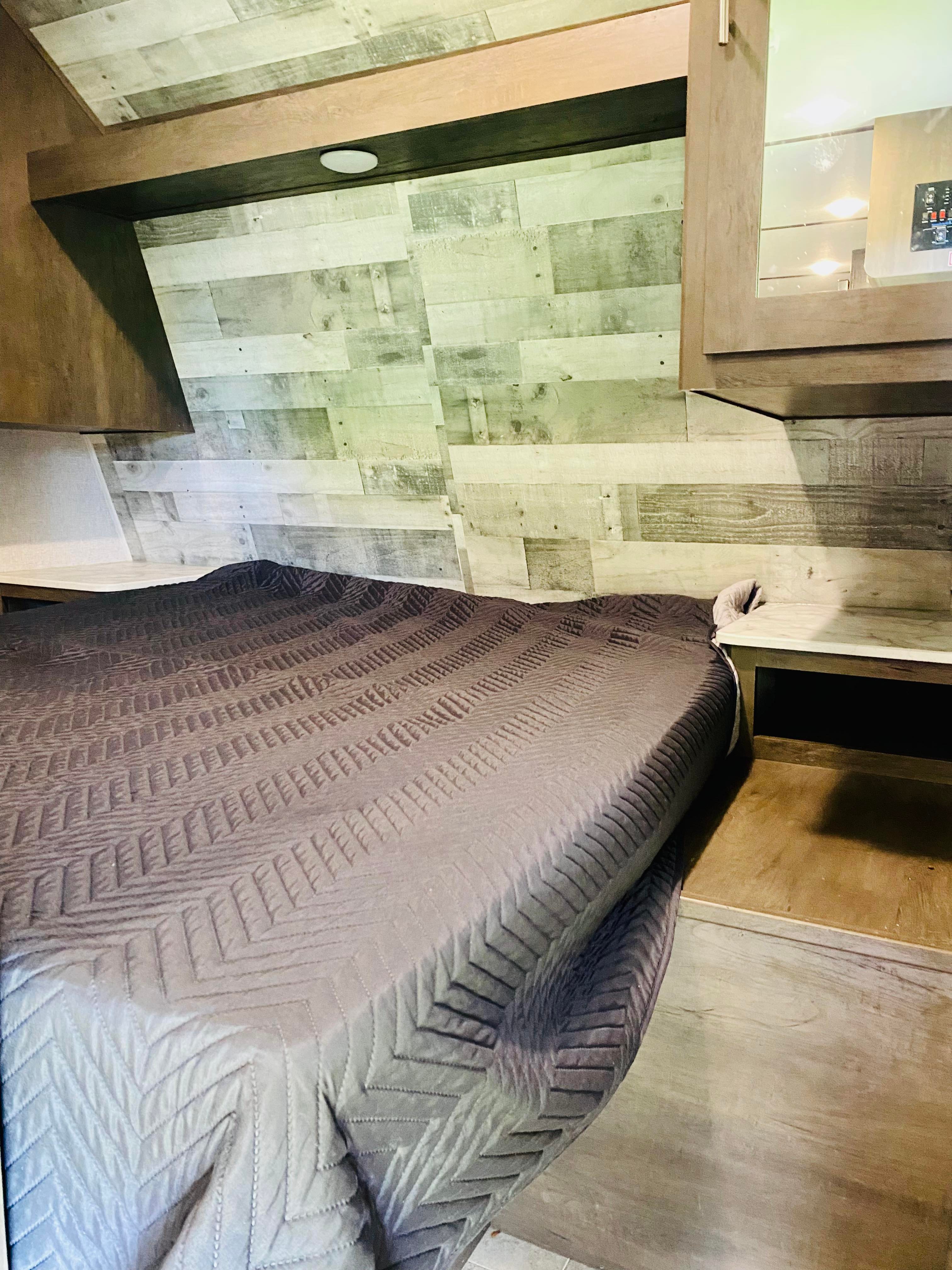 Cozy RV rental bedroom featuring a comfortable bed with a patterned comforter, wood-planked accent wall, and side shelves.. Coleman Lantern 2021