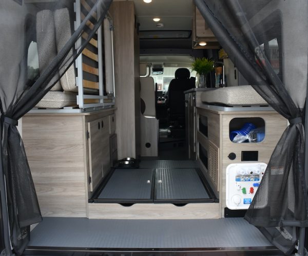 Open rear door of an RV rental reveals a cozy interior with mesh screens, bed, kitchen, and utility panel for travel.. Winnebago Solis 2022