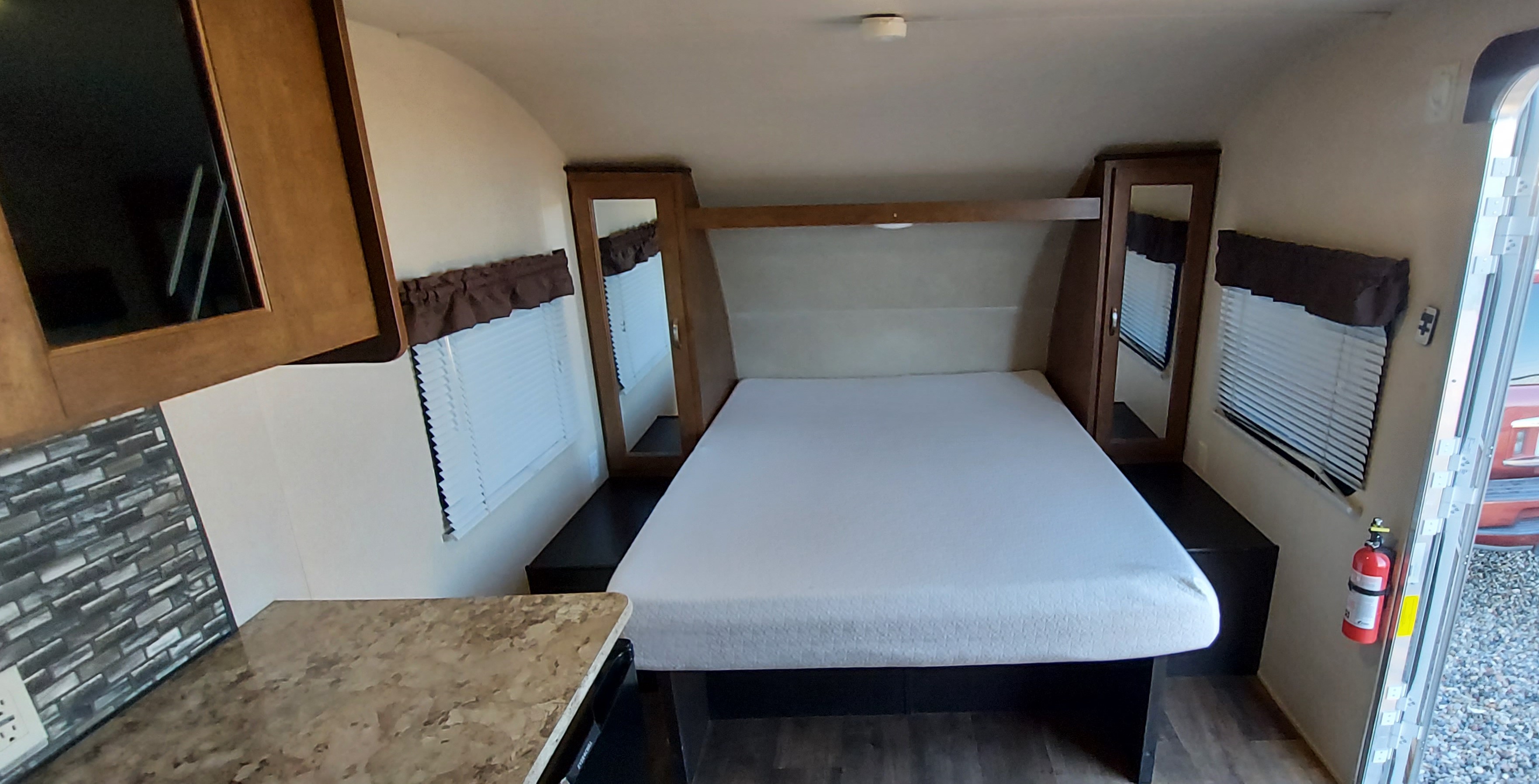 Interior of an RV rental: a cozy bedroom with a white mattress, side cabinets, and a compact kitchen counter on the left.. Forest River Salem Cruise Lite 2017