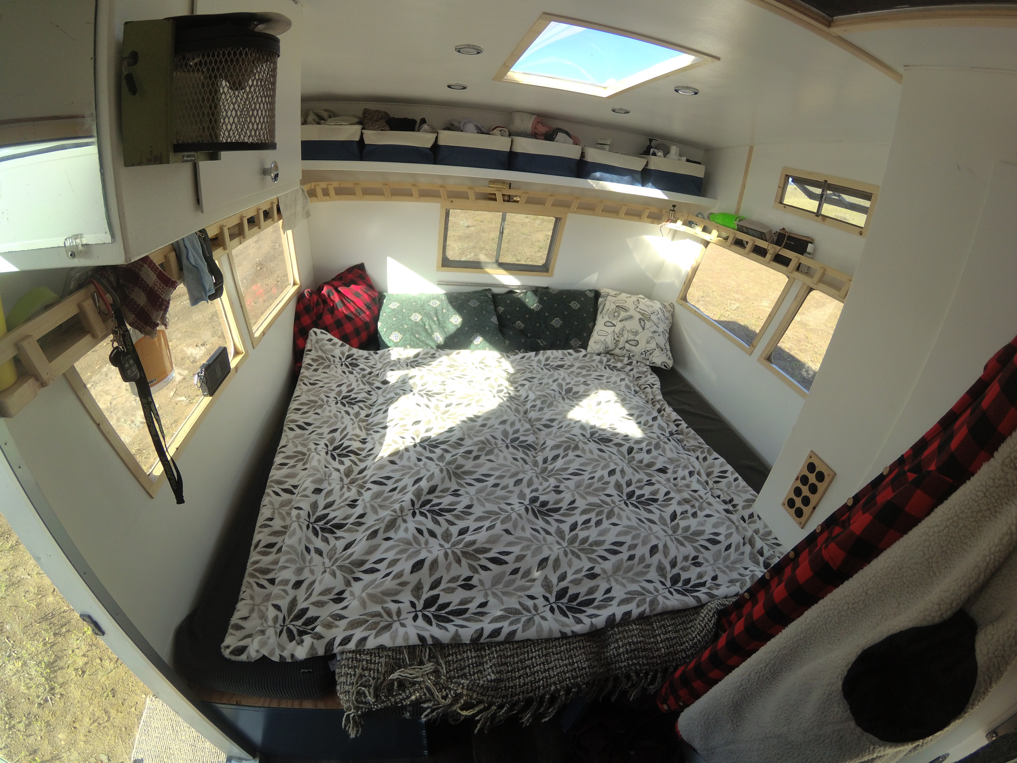 Spacious RV rental bedroom with a leaf-patterned bed, multiple windows, and bright skylight, showcasing a comfortable mobile living space.. Shasta Airflyte 1969