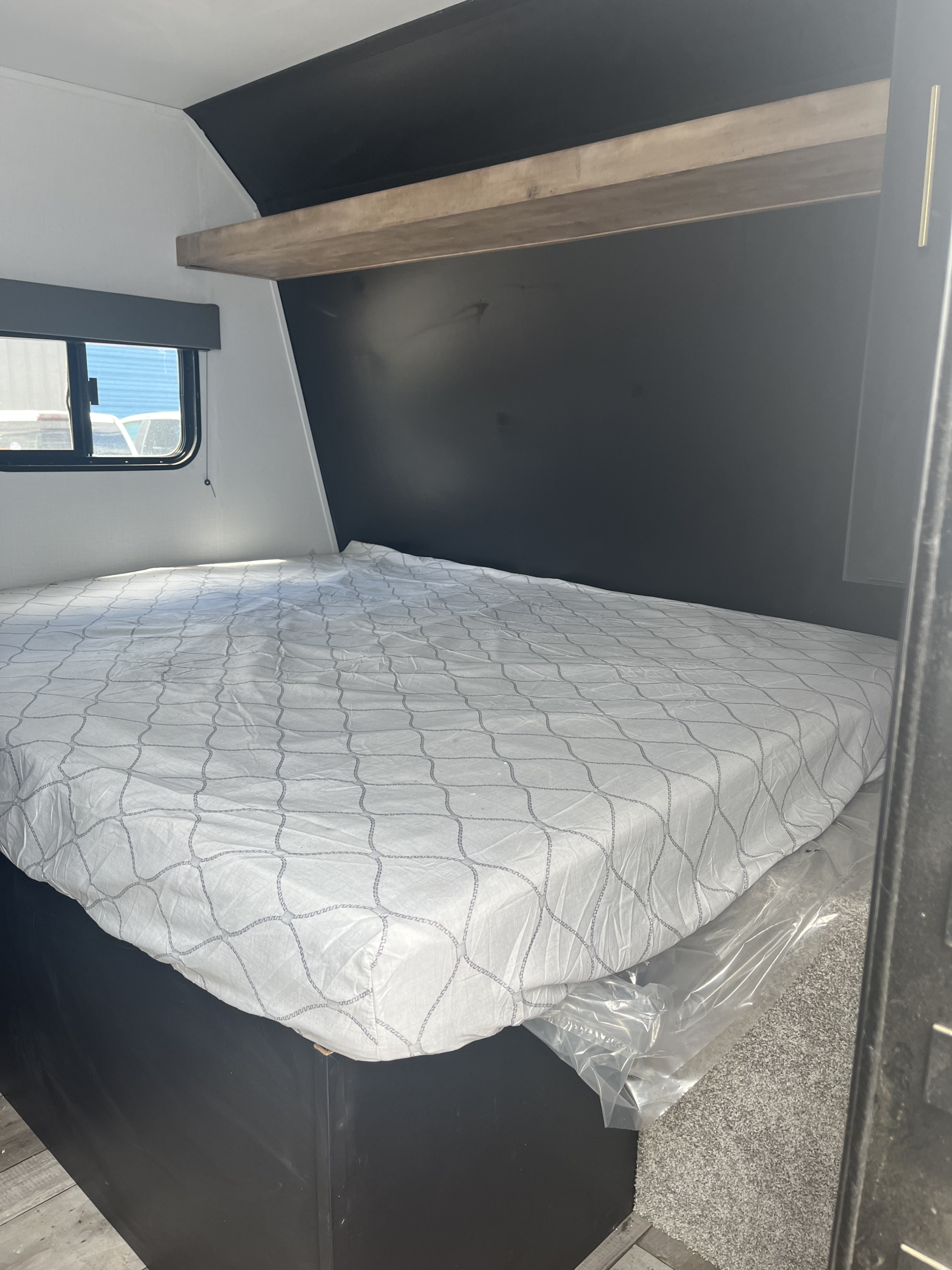 Clean RV rental bedroom featuring a bed with white patterned sheets & clear mattress protection. Includes a window and overhead shelf.. Keystone RV Springdale 2022