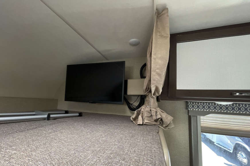 This RV rental interior features a cozy overhead bunk bed with a mounted TV, a ladder, and window blinds.. Thor Freedom Elite 2017