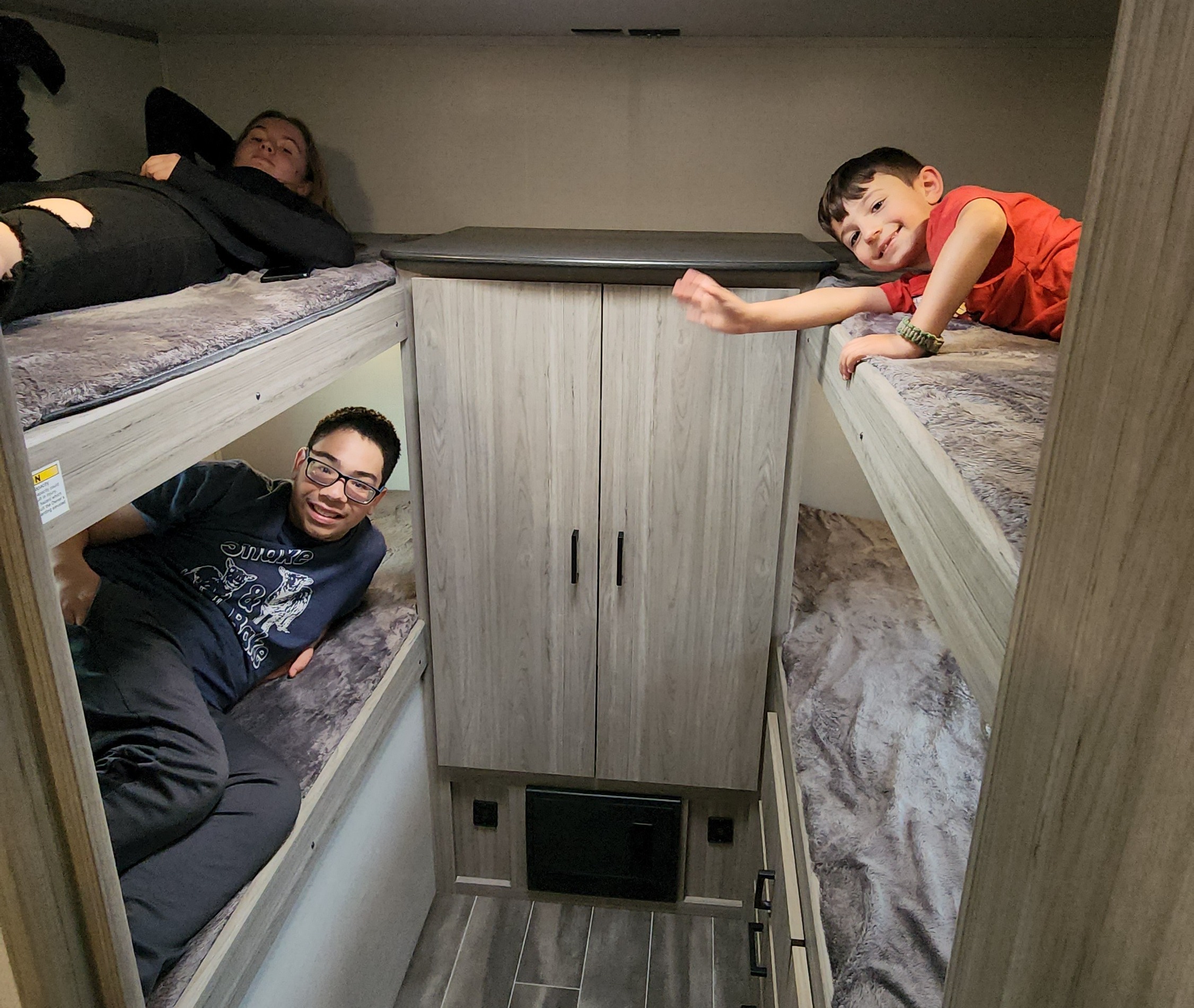 Three people lounging in the bunk beds of an RV rental, a comfy space for family camping trips and relaxation.. Keystone RV Passport SL 2022