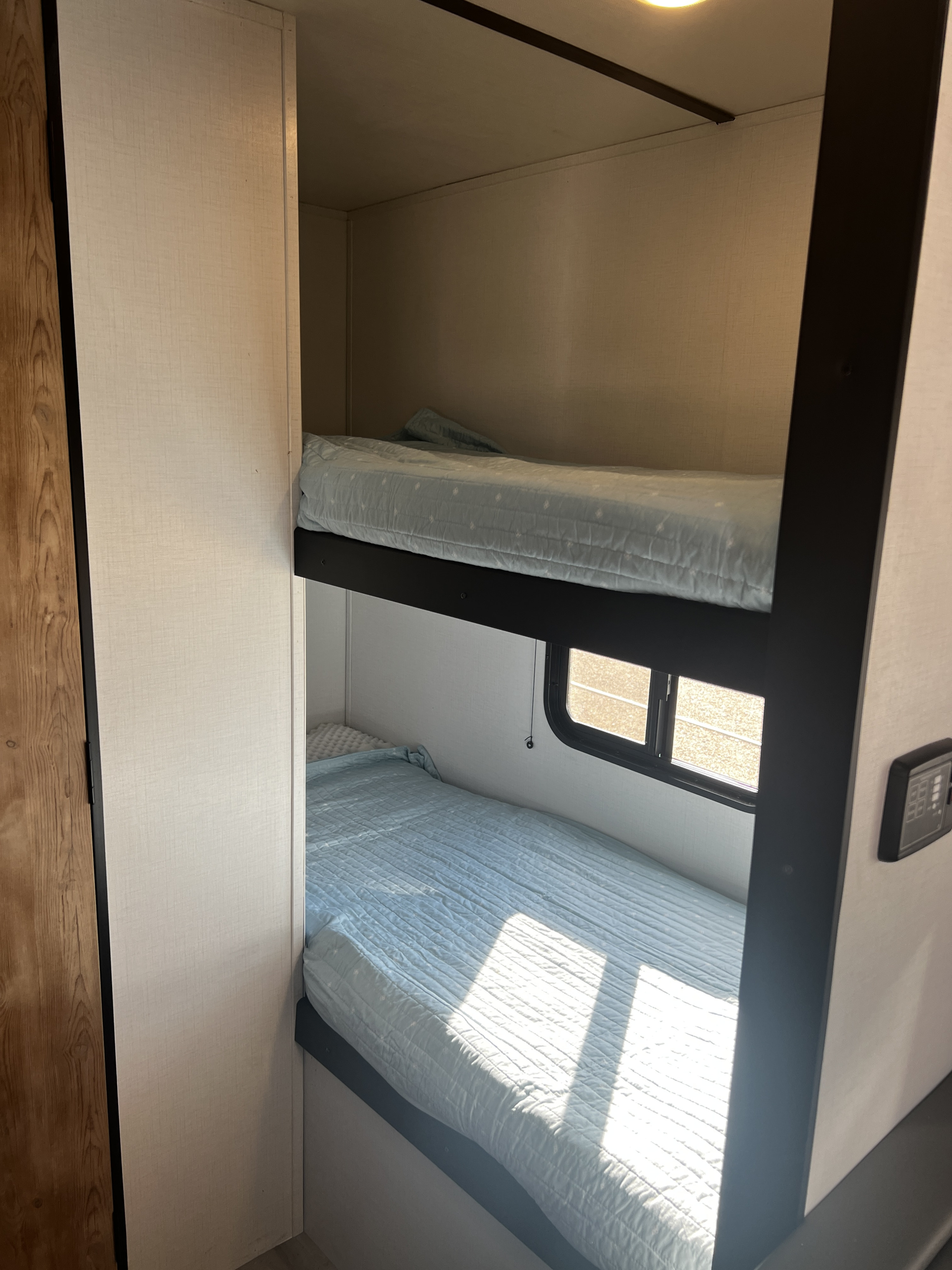 Inside an RV rental: Two cozy bunk beds with light blue bedding. Natural light streams through the lower bunk's window.. Keystone Springdale 1800BH 2022