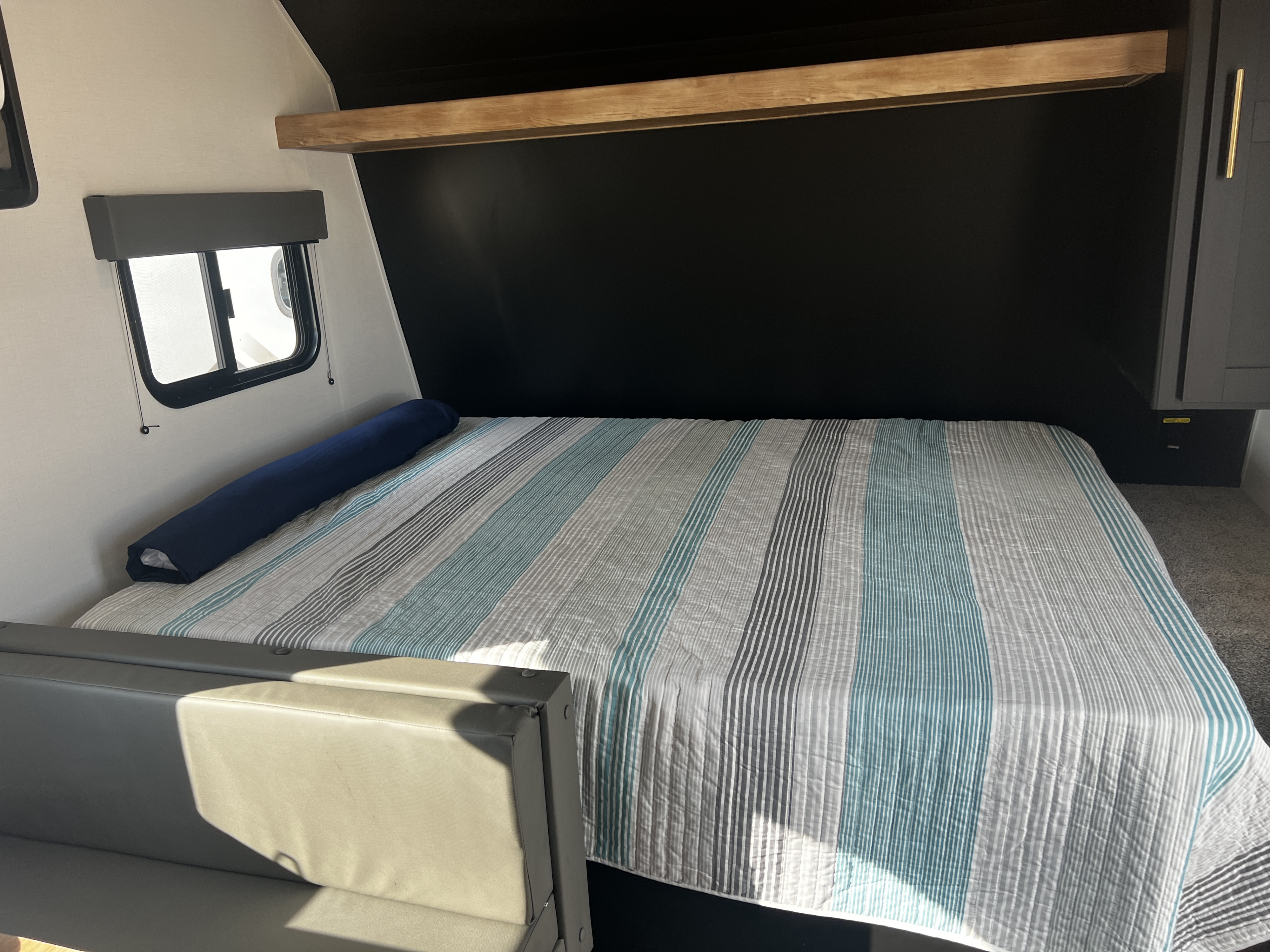 Cozy RV rental interior: A bed with striped quilt, side window, and wood shelf, offering comfortable sleeping.. Keystone Springdale 1800BH 2022