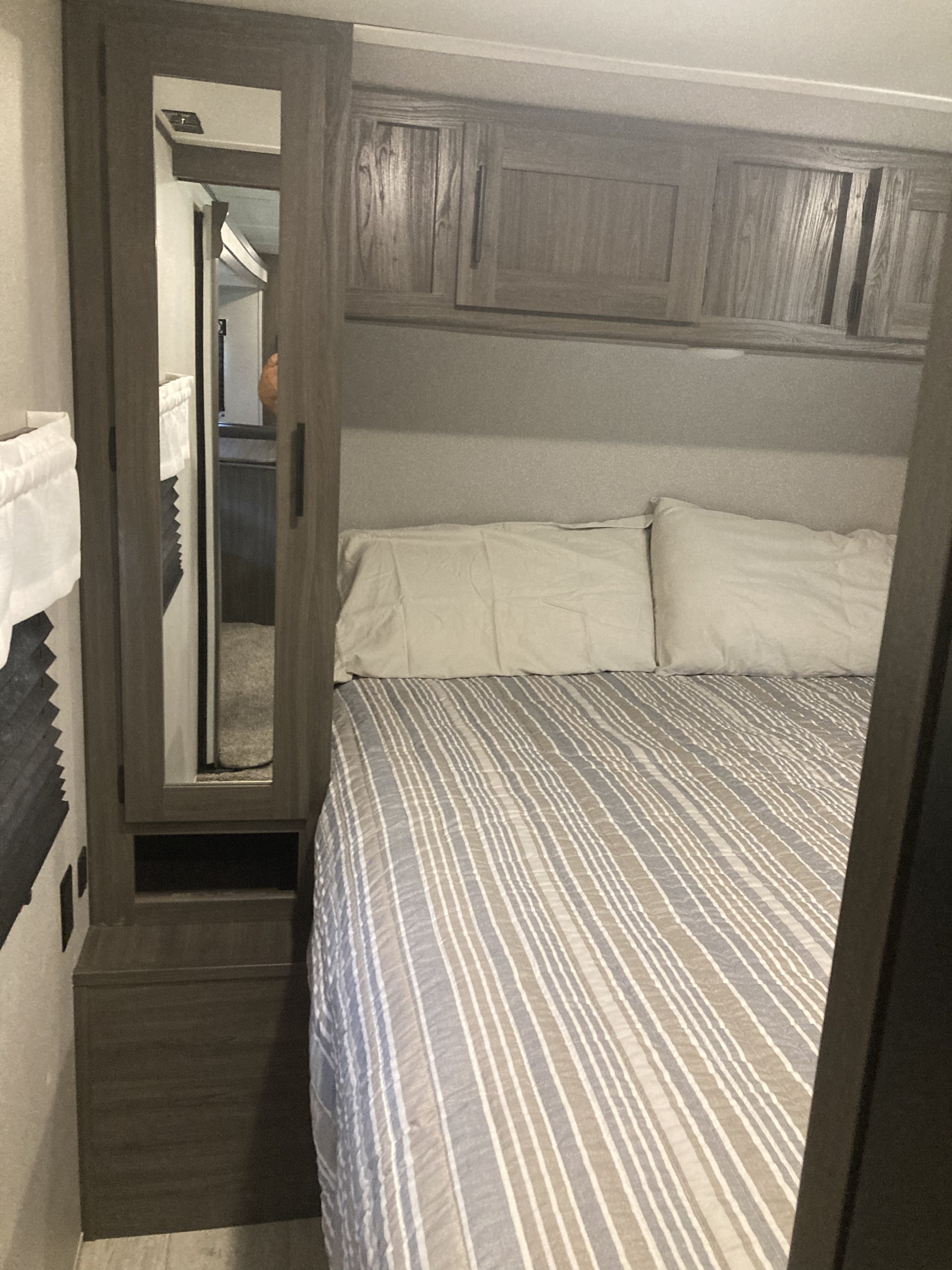 Inside an RV rental, a cozy bedroom with a striped bed, pillows, overhead storage, and a mirrored closet on the left.. Forest River Shasta 2021