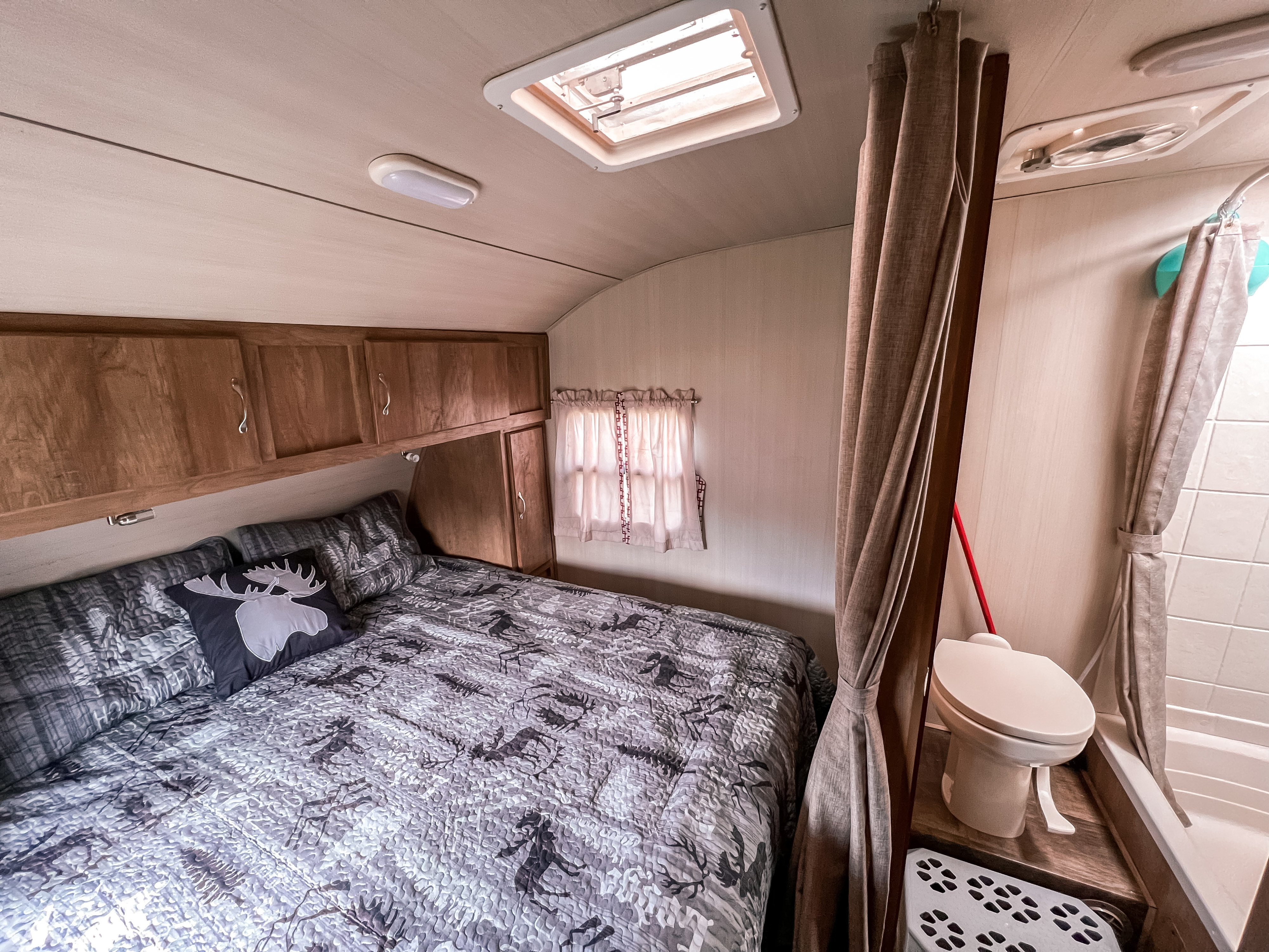 Cozy RV rental bedroom featuring patterned bedding, overhead storage, and an attached compact bathroom for travel comfort.. Gulf Stream Cruiser 2017
