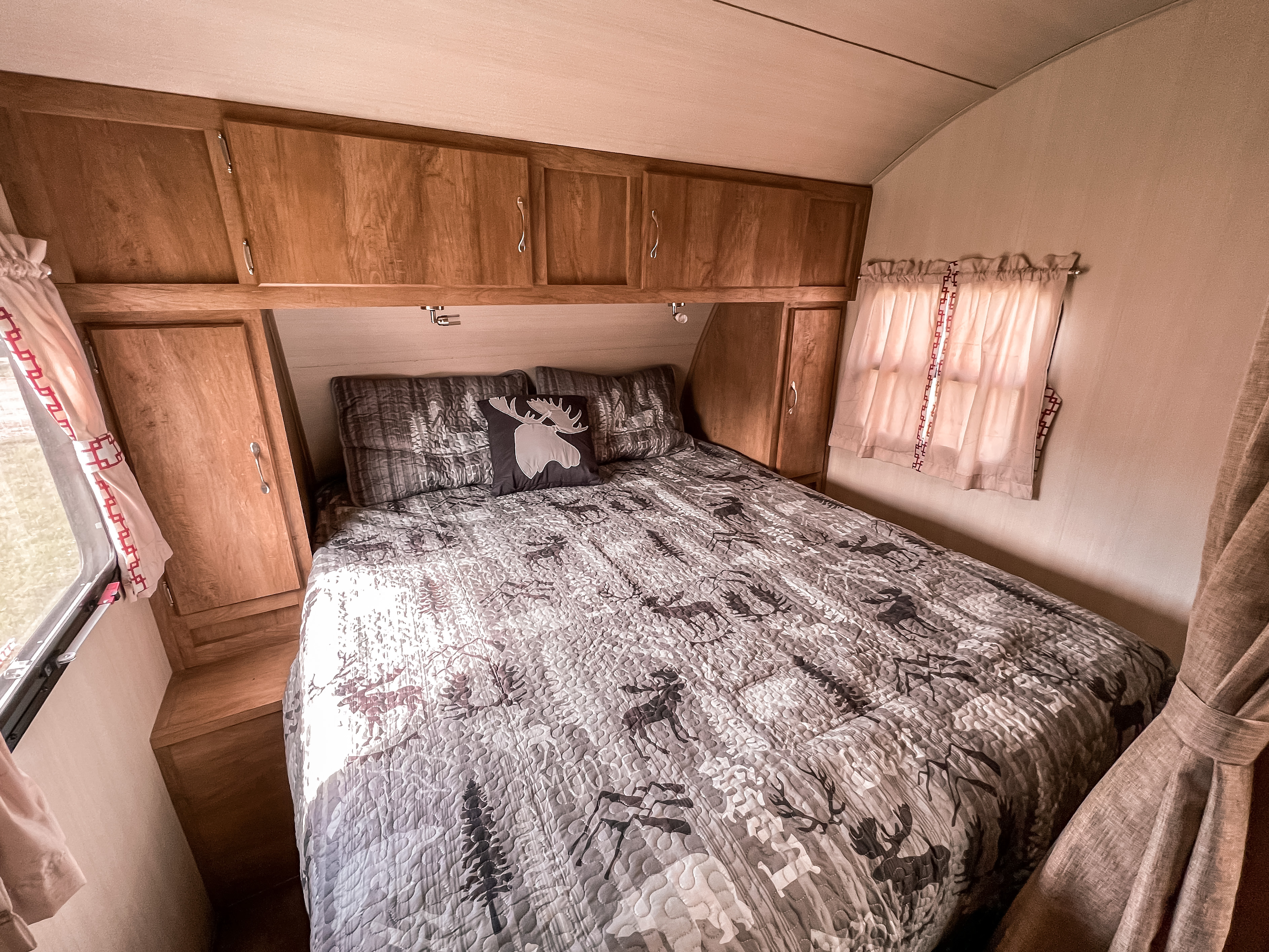 Cozy RV rental bedroom with moose-themed bedding, overhead cabinets, and patterned curtains, providing a comfortable space.. Gulf Stream Cruiser 2017