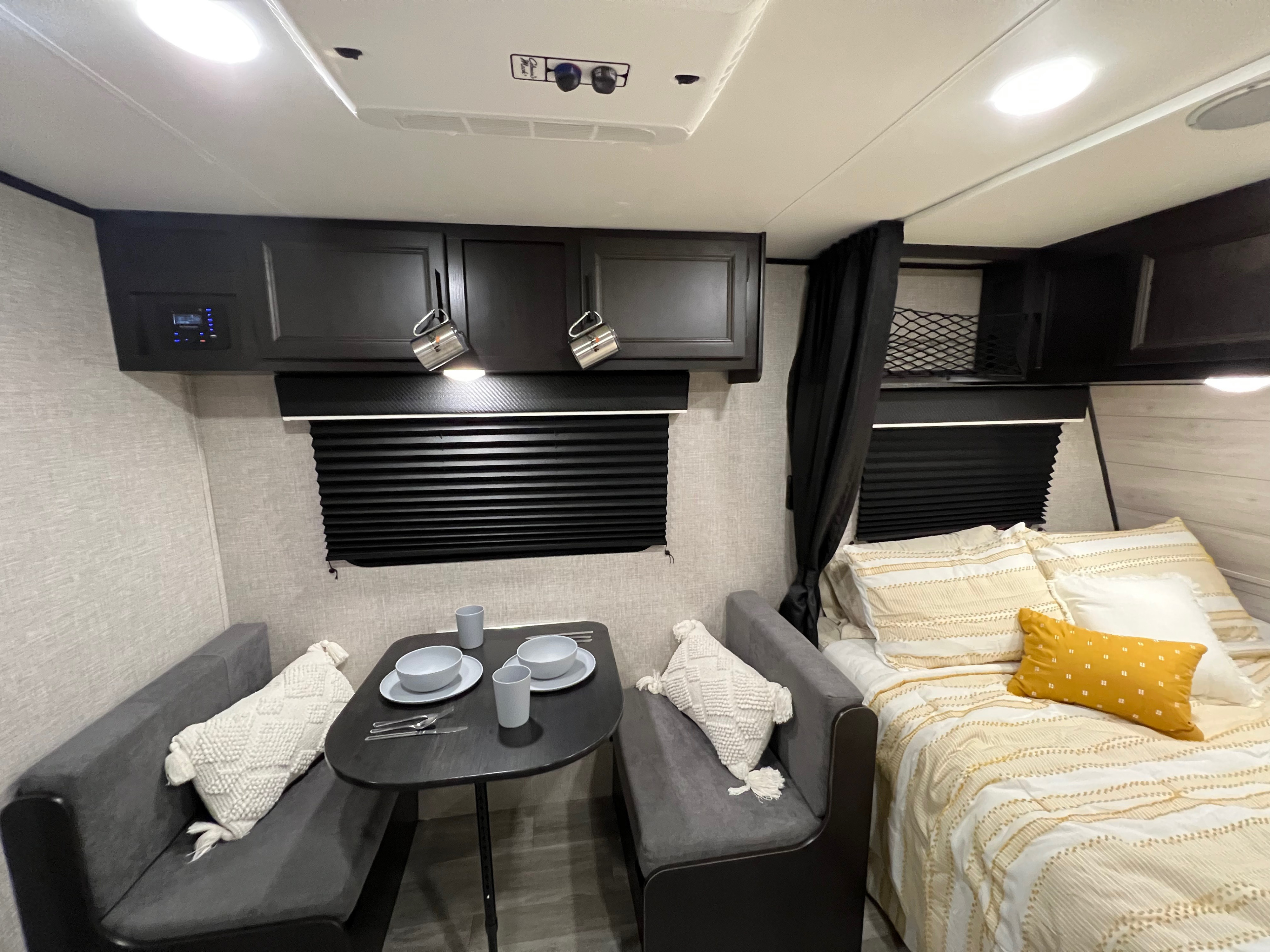 This RV rental interior features a compact dinette with table and benches, plus a cozy bed with yellow bedding.. Jayco Other 2022