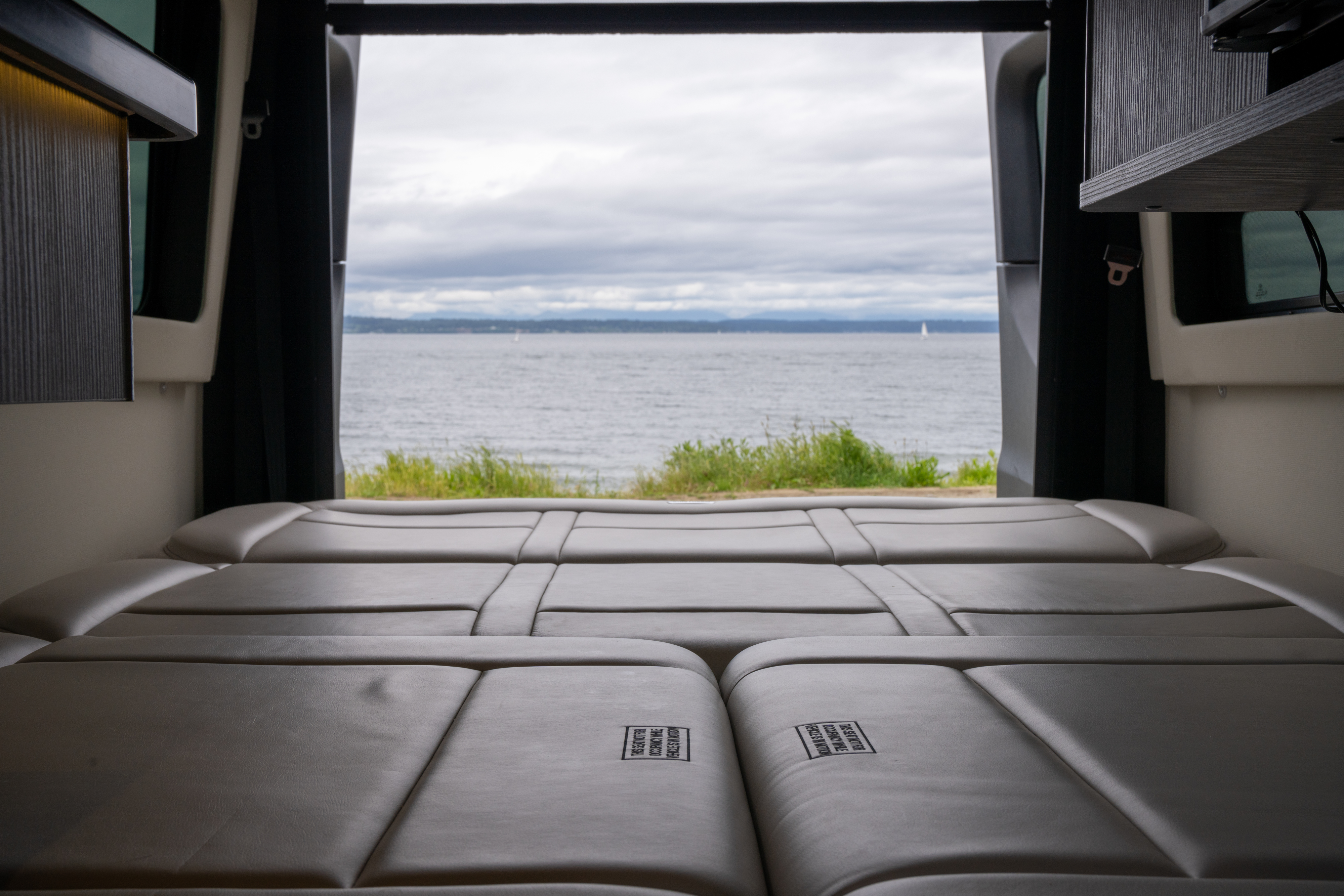 RV rental interior: comfy bed with a scenic ocean view. Enjoy the perfect van life escape by the water.. Airstream Interstate 2020