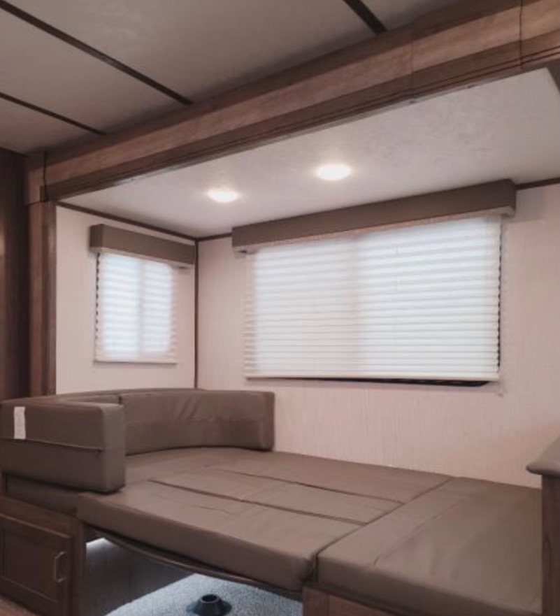 RV rental interior showing a convertible sofa bed, two windows with white blinds, and recessed ceiling lights, providing comfort.. Keystone RV Passport SL 2021
