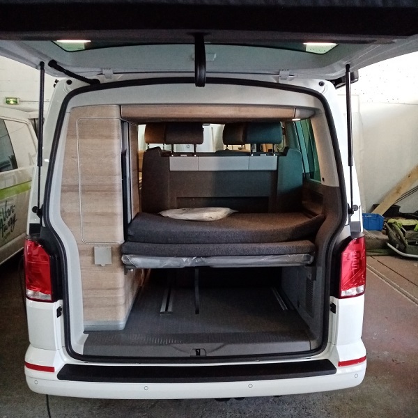 Inside this RV rental: a versatile camper van setup with a comfortable bed and built-in storage, viewed from the rear.. Volkswagen California Coast T6.1 DSG7 2022