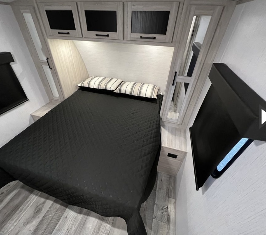 RV rental bedroom with a comfortable black bed, light wood overhead cabinets, and mirrored storage on each side.. Heartland RVs Sundance Ultra Lite 2021