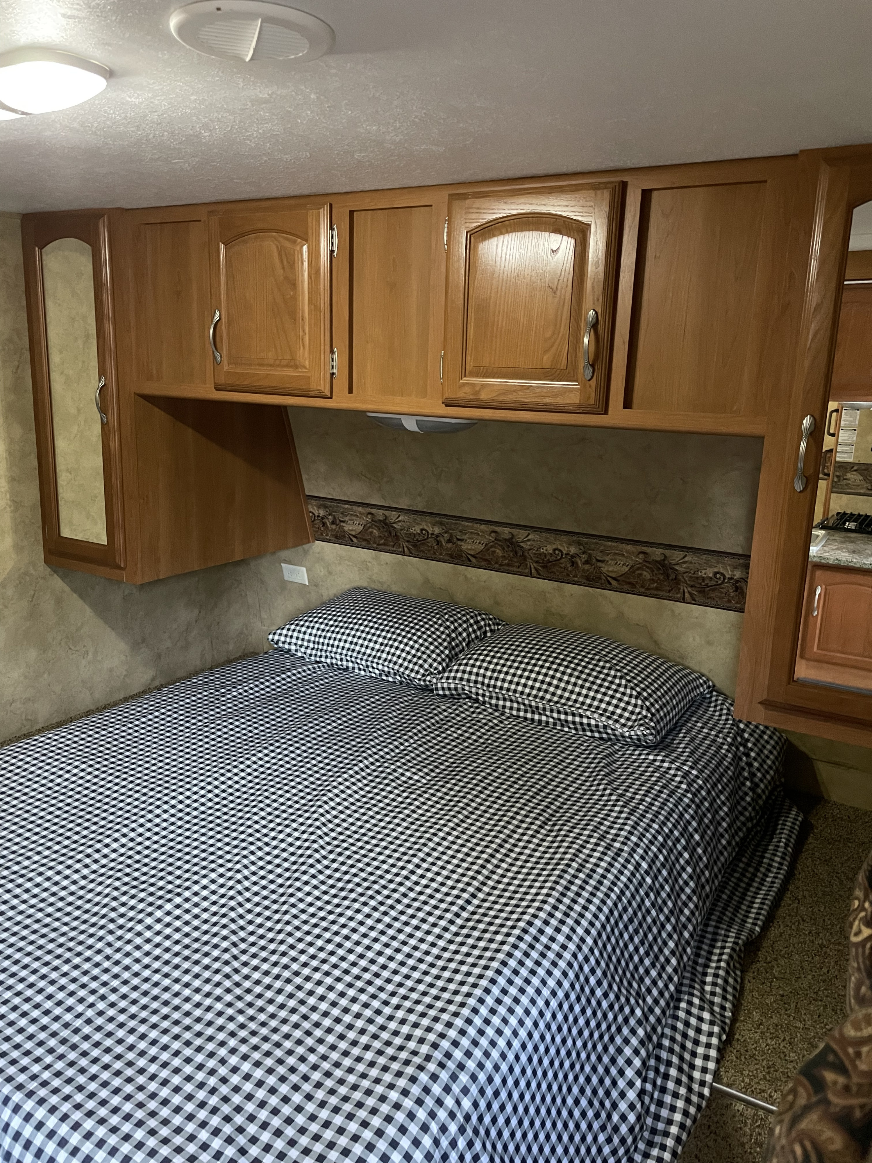 Cozy RV rental bedroom with black and white gingham bedding, overhead storage, and mirrored cabinets.. Keystone RV Cougar 2010
