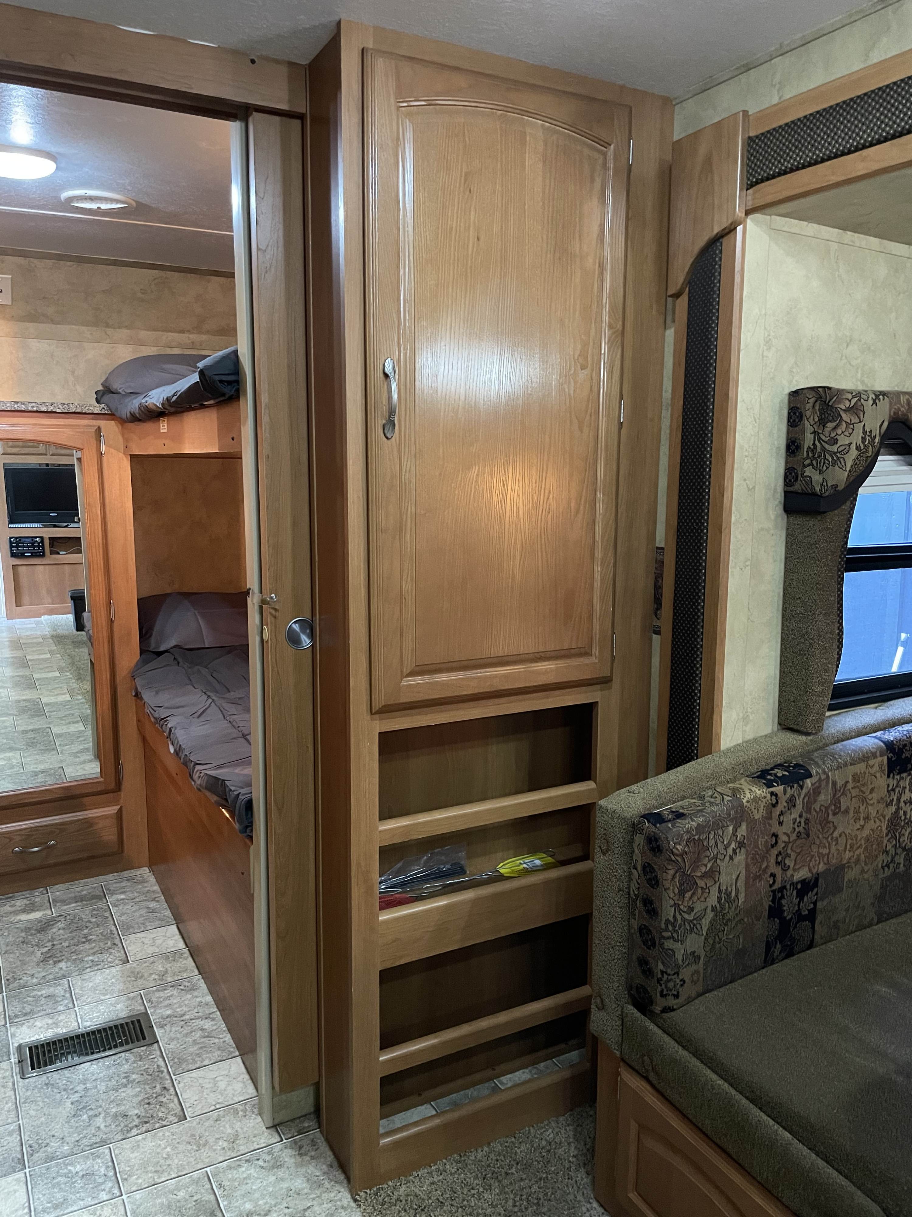 RV rental featuring a bunk bed setup with storage, a large wooden cabinet, and patterned seating.. Keystone RV Cougar 2010