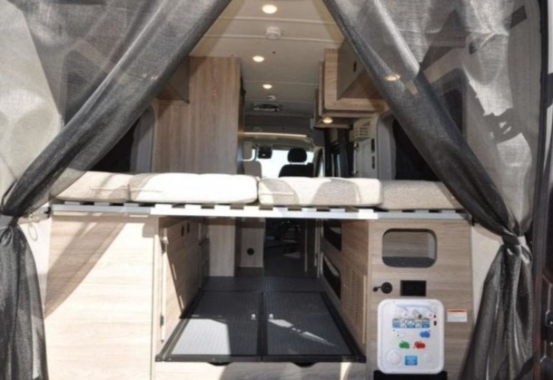 Camper van interior, rear view: elevated bed above flexible storage. Explore your next RV rental adventure.. Winnebago Solis 2022