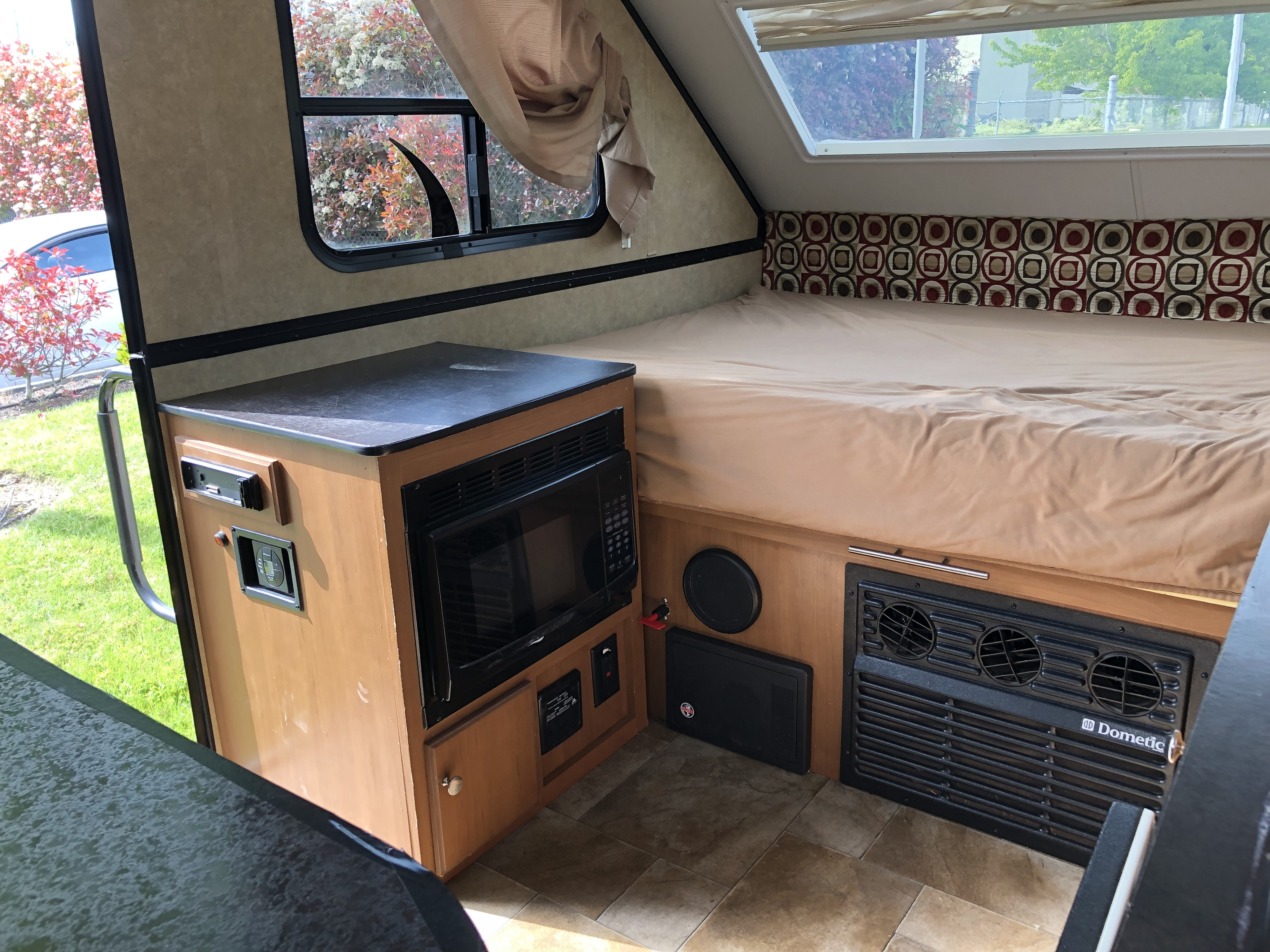 Compact A-frame RV rental interior with a cozy bed, microwave, and Dometic furnace/vent. Tiled floor and window views.. Starcraft Comet 2015