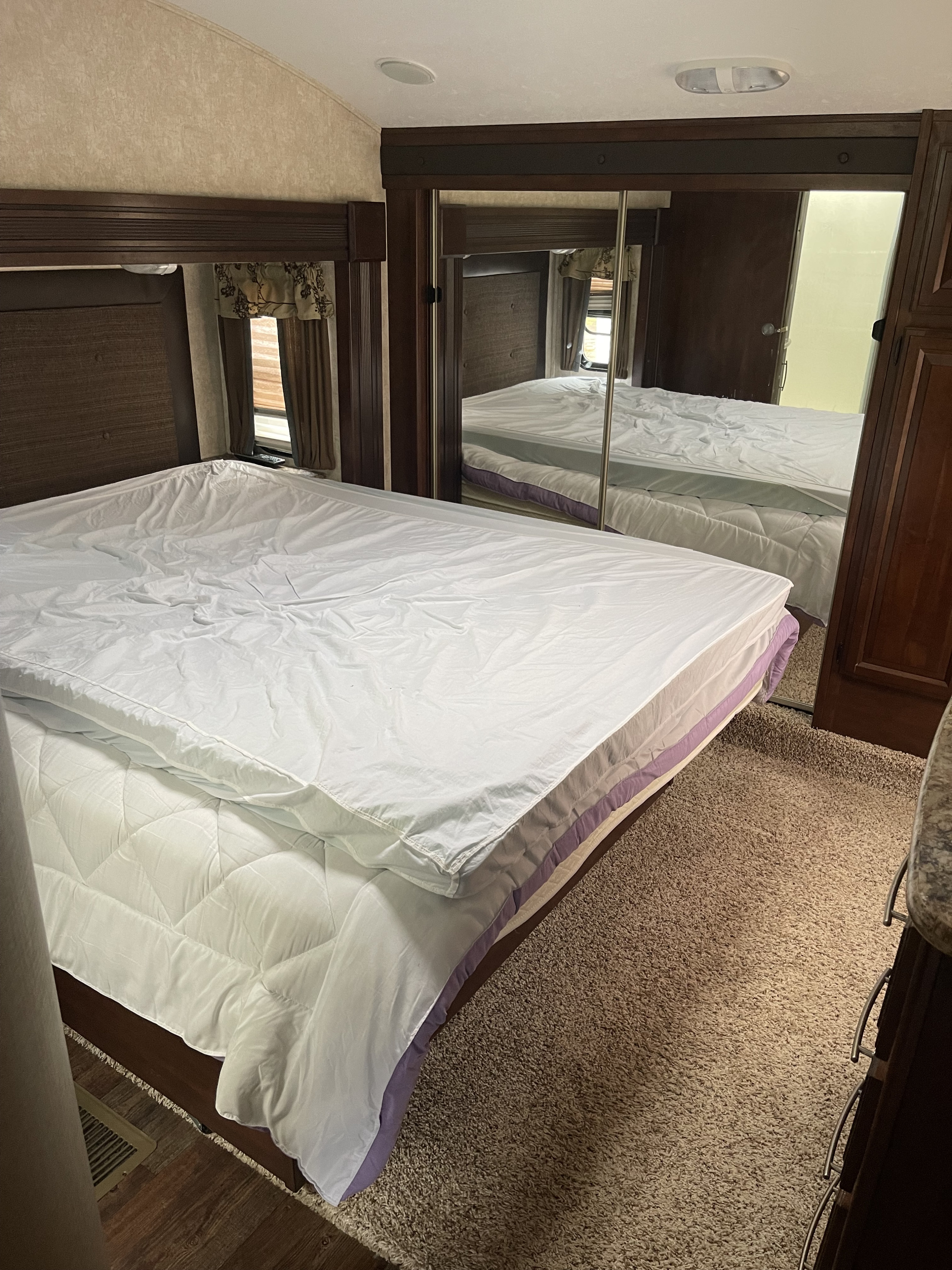 Comfortable RV rental bedroom featuring a white bed, mirrored wardrobe, and warm wood finishes.. Keystone RV Cougar 2015