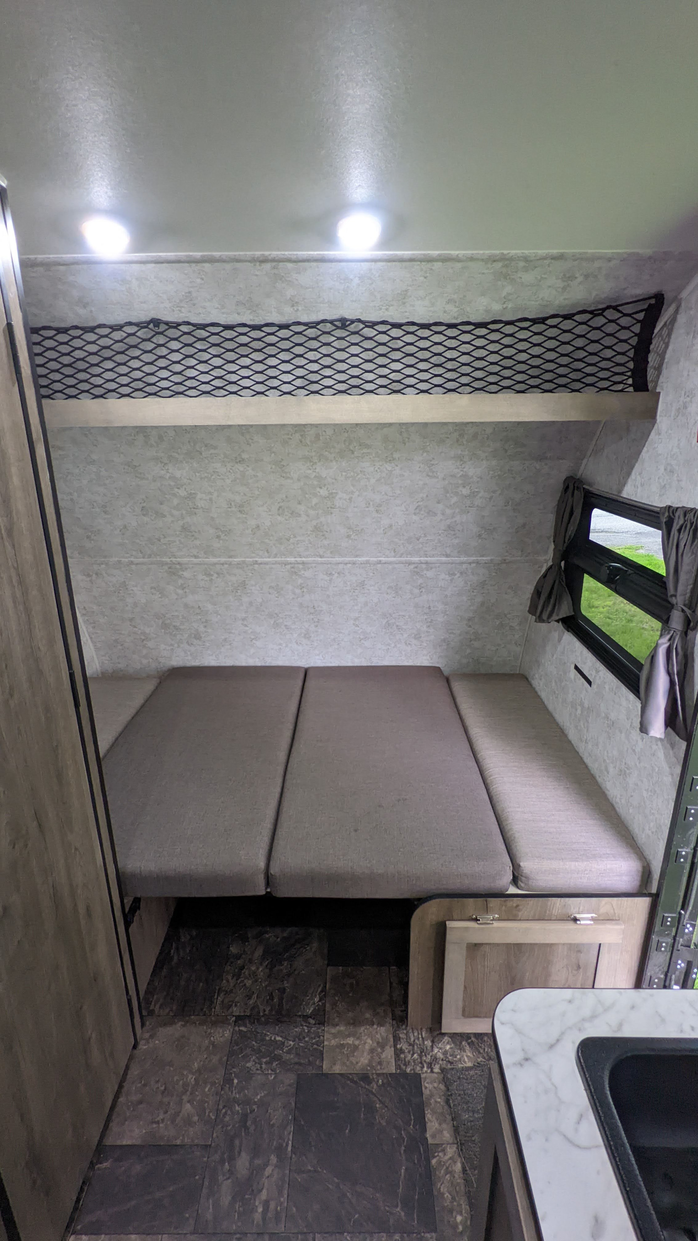 RV rental interior: A versatile bed/seating area, overhead storage net, window, and partial sink are visible. Ready for adventure!. Prolite RV Evasion 16 2022