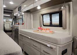 Step into comfort: This RV rental interior features a bright, modern living space with a bed, kitchen counter, and storage, overlooking a scenic view.. Dodge Thor 3500 2022