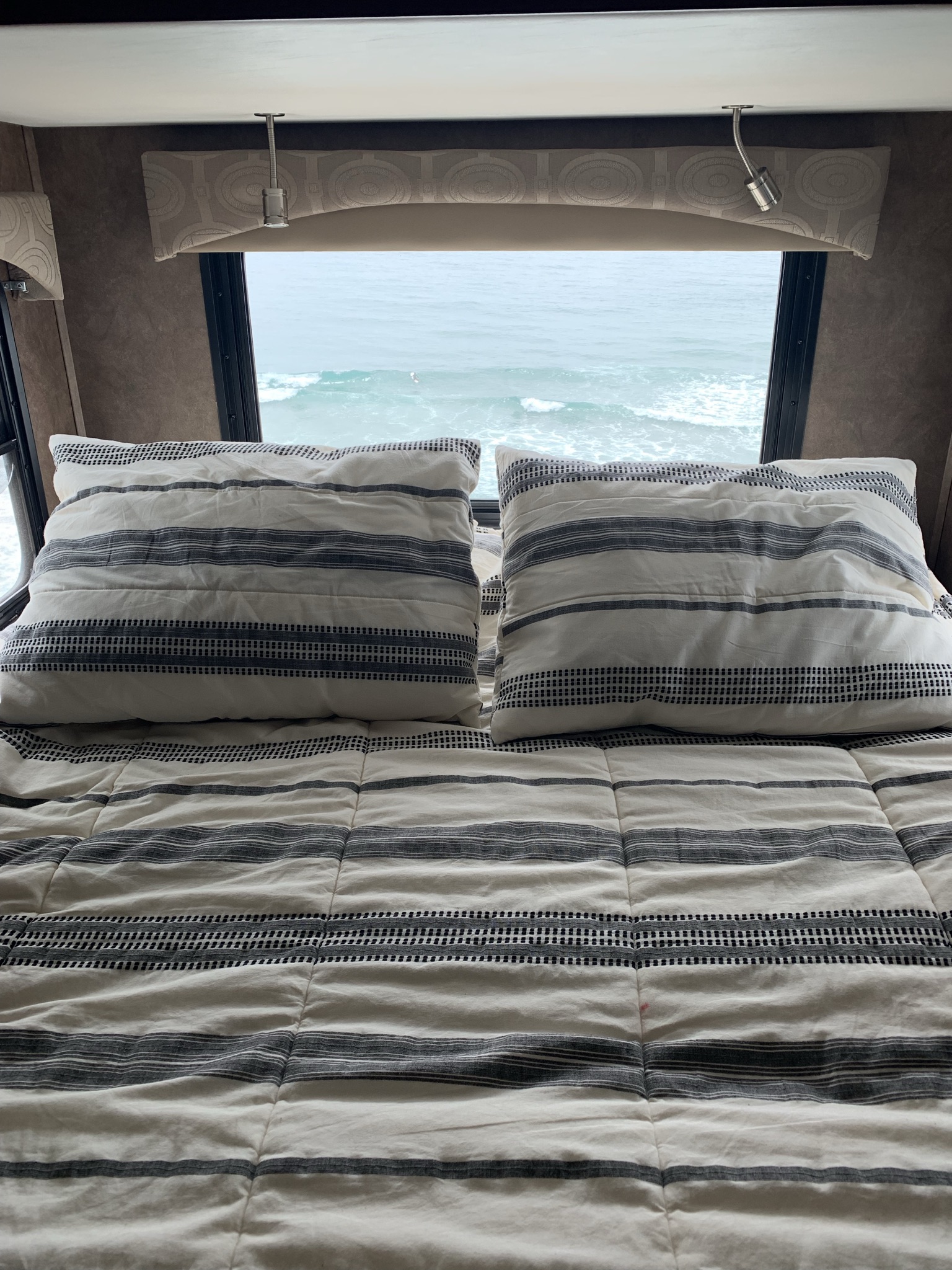 Relax in an RV rental with an ocean view! Cozy bed with striped bedding and reading lights provide comfort.. Forest River Forester 2501TS 2015