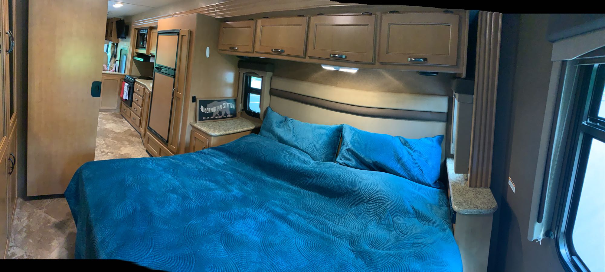 Cozy RV rental interior showing a comfortable bedroom with blue bedding and a glimpse of the kitchen.. A.C.E. 27.1 2015