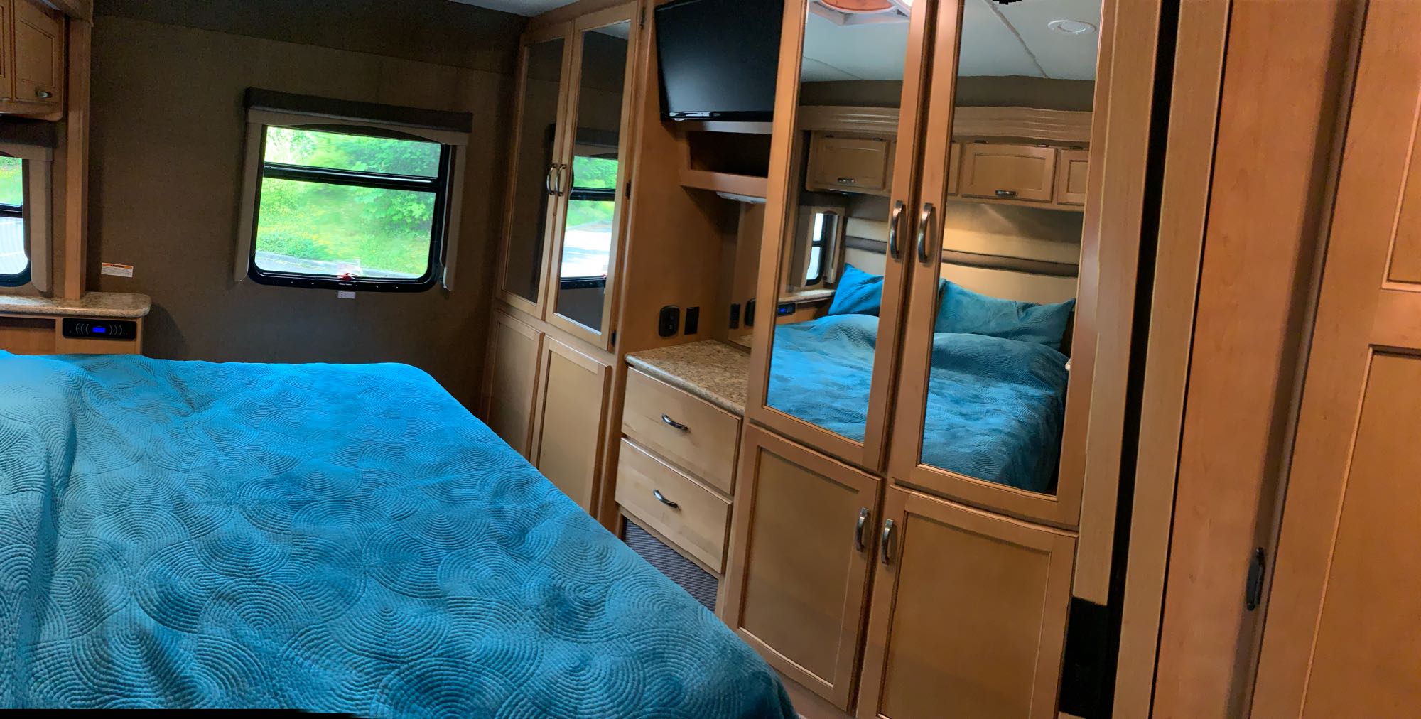 Inside a comfortable RV rental bedroom, featuring a vibrant blue bed, mirrored closets, and a view of nature.. A.C.E. 27.1 2015