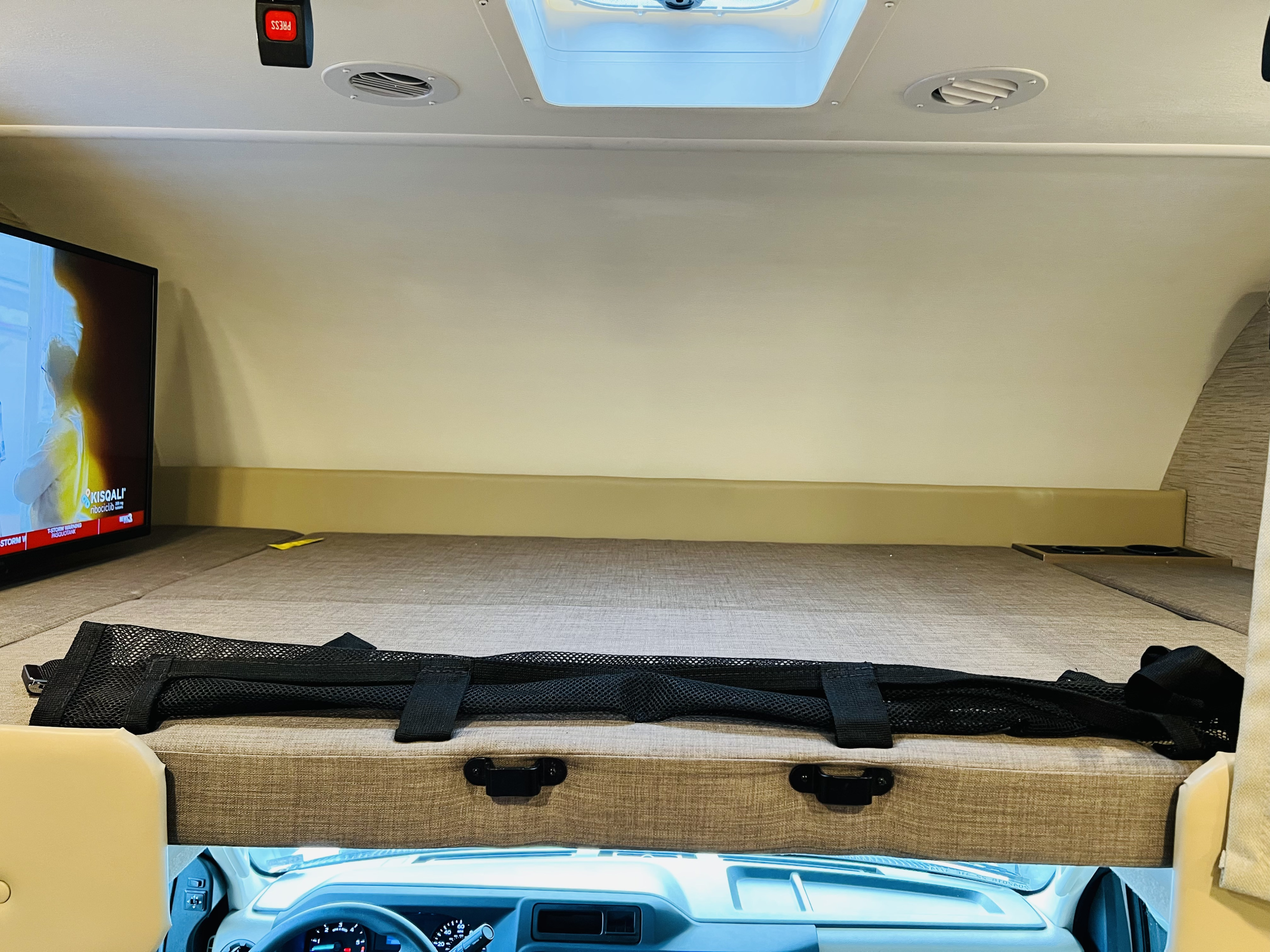 Overhead bunk and cab area of an RV rental, featuring a TV and mesh storage. Perfect for family road trips.. Four Winds 31E 2022