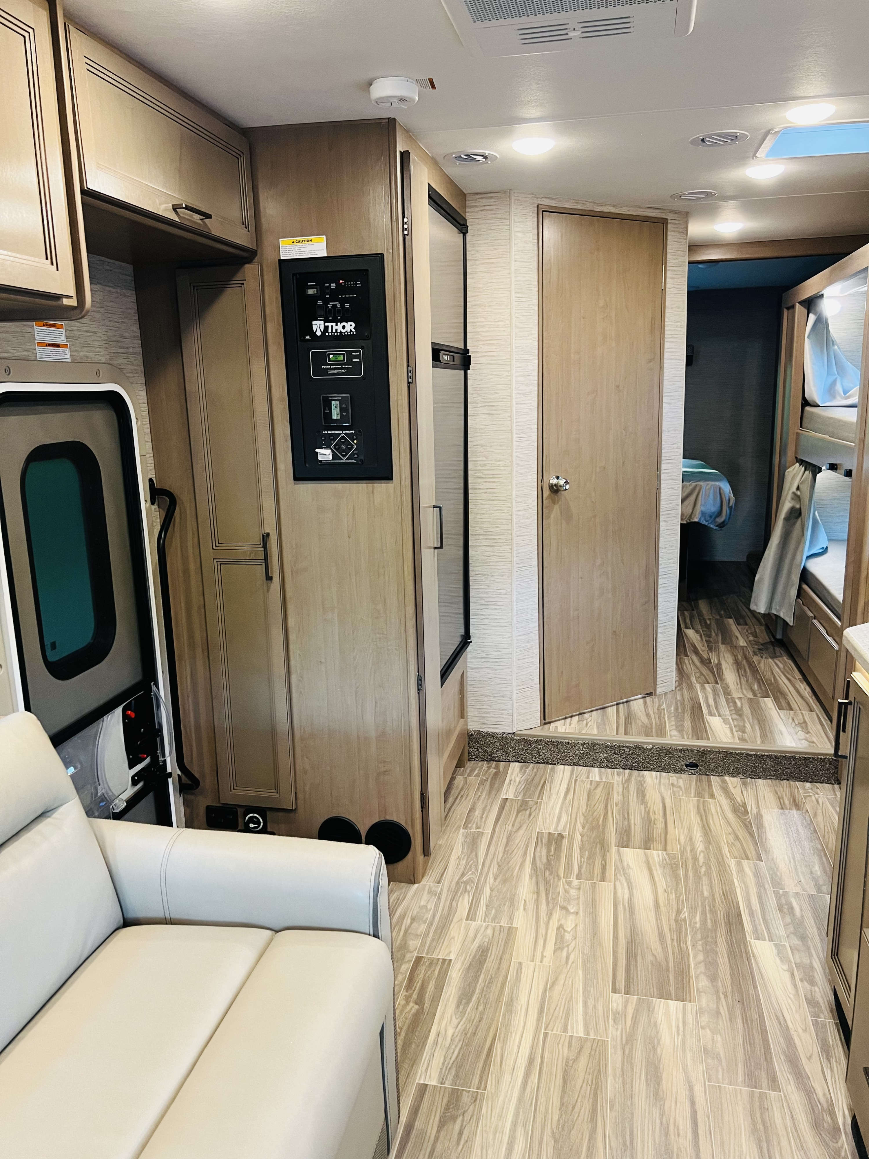 Spacious RV rental interior with sofa, THOR control panel, modern wood flooring, and bunk beds in rear.. Four Winds 31E 2022