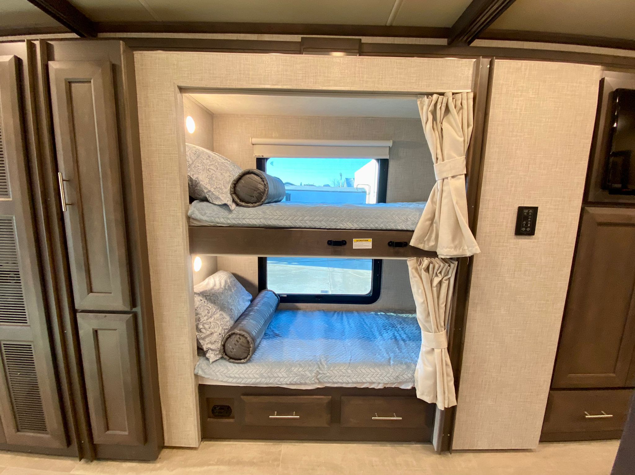 Comfortable **RV rental** interior featuring neatly made stacked bunk beds with windows and wood cabinetry.. Thor Motor Coach Aria 2022
