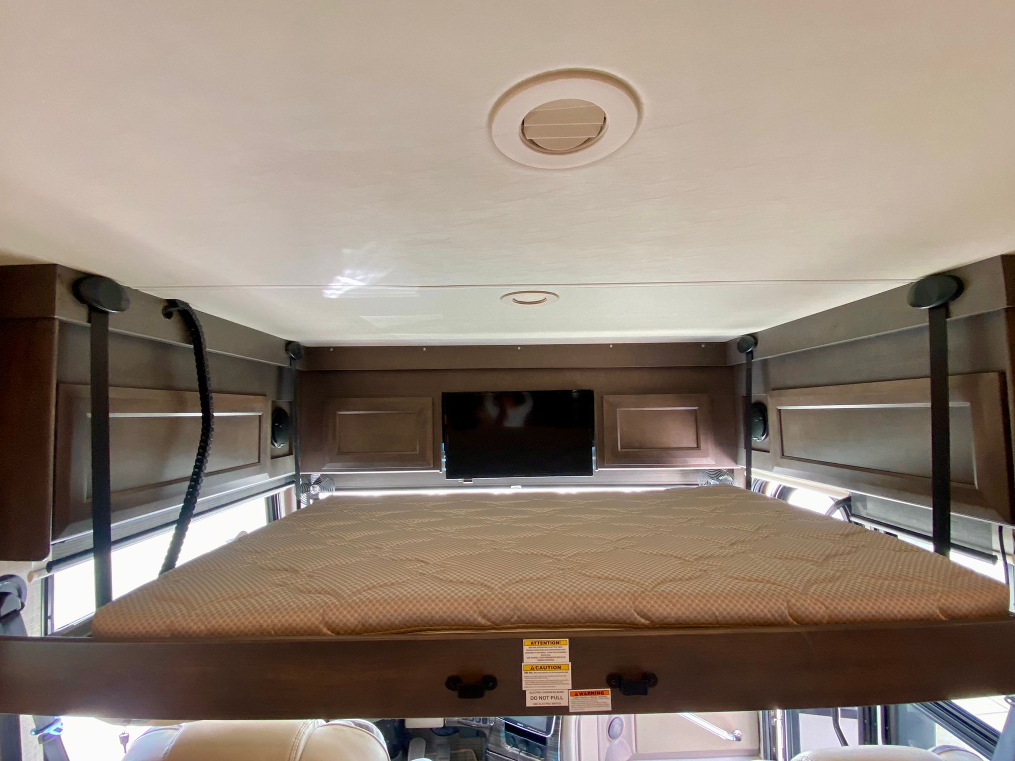 RV rental interior: A lowered drop-down bunk bed with mattress and TV. Note warning labels for safe use.. Thor Motor Coach Aria 2022