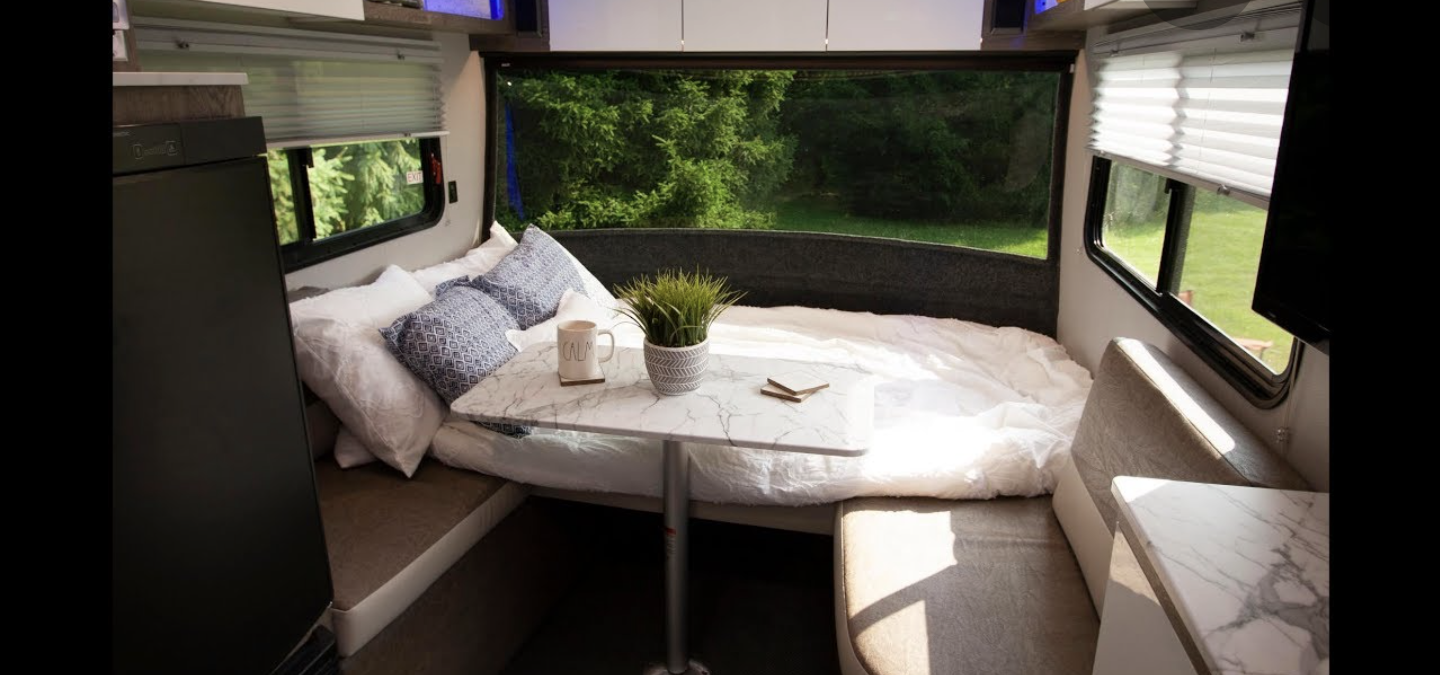Cozy RV rental interior with a comfortable bed, dinette table, and large window view. Perfect for mobile living.. Intech Sol Horizon Rover 2022