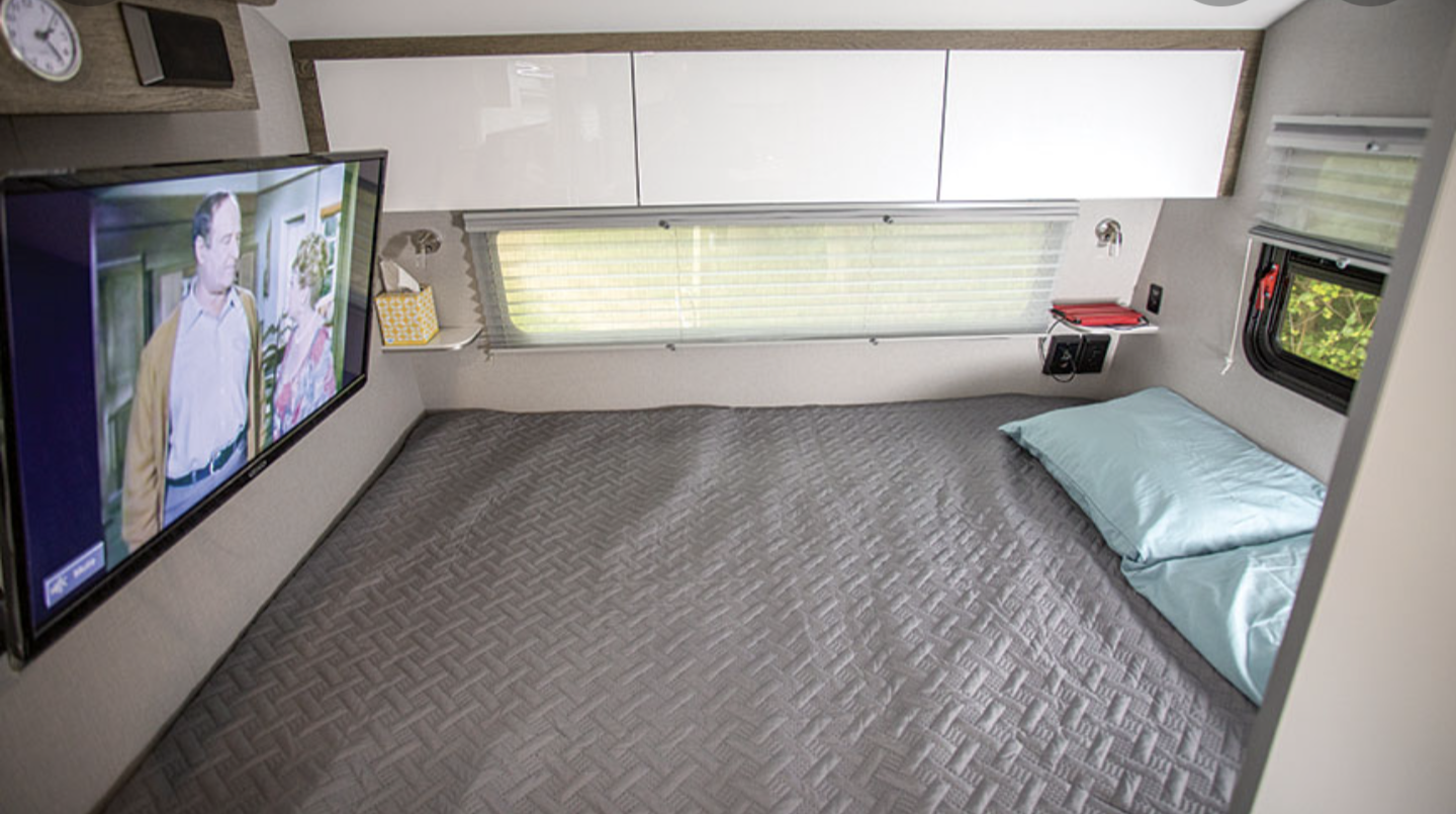 Compact RV rental interior featuring a comfortable bed with a quilted cover, wall-mounted TV, and smart storage solutions.. Intech Sol Horizon Rover 2022