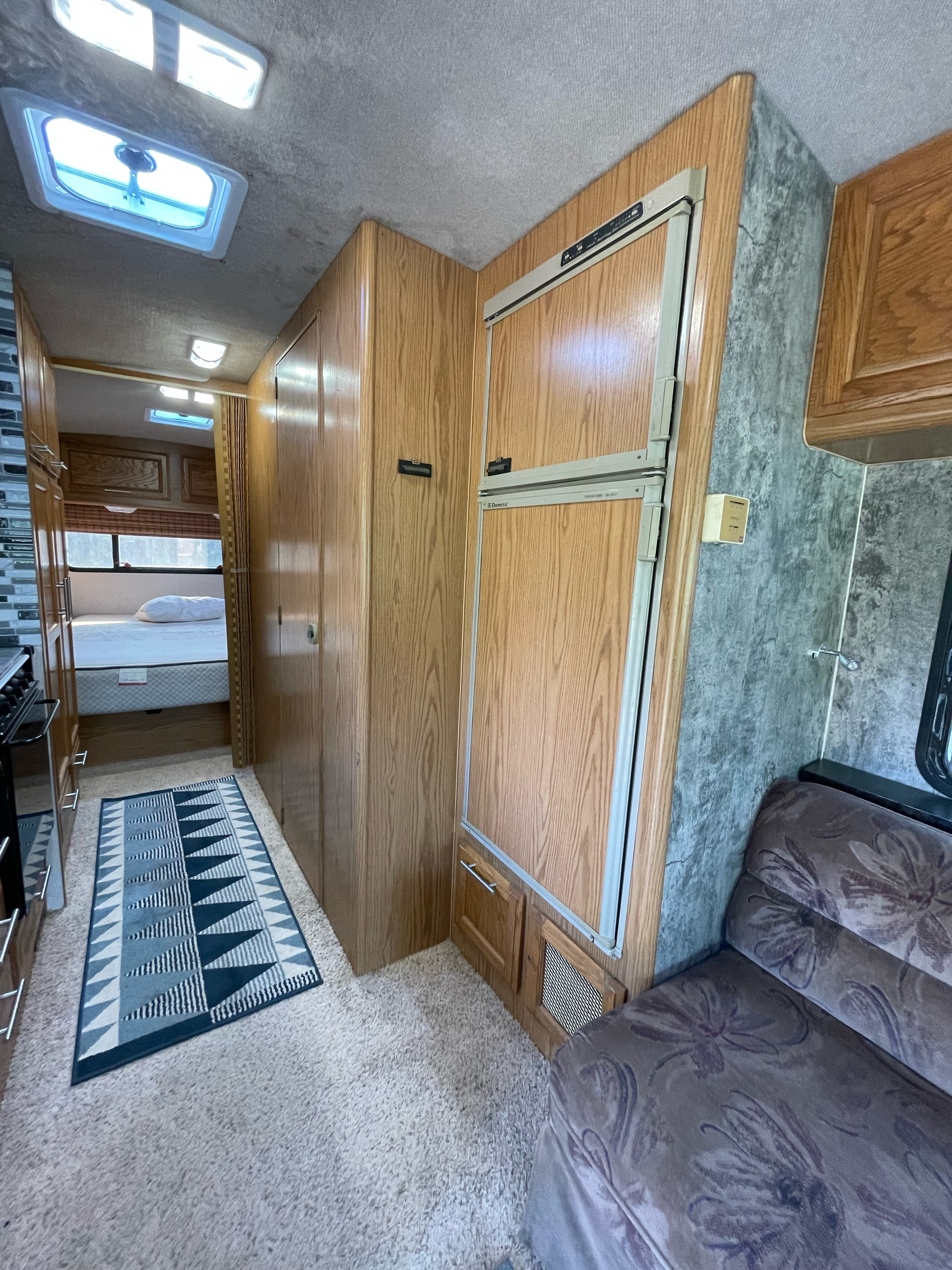 RV rental interior featuring a compact kitchen, hallway to bedroom, refrigerator, and patterned sofa.. Fleetwood Bounder 1992