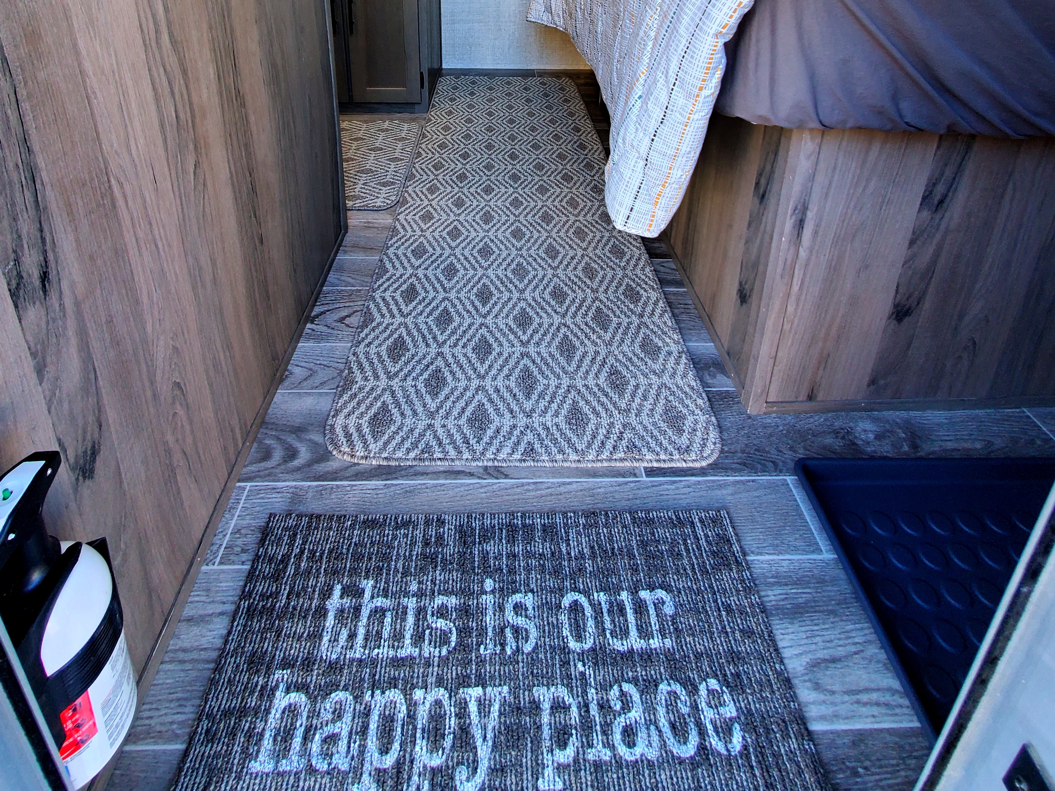 An inviting RV rental interior with "this is our happy place" mat, patterned runner, and bed area. Fire extinguisher seen.. Gulf Stream Ameri-Lite Super Lite 2021