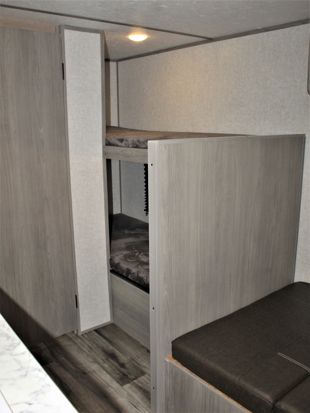View inside an RV rental showing stacked bunk beds with dark mattresses, light wood storage, and seating.. East to West lantern LT 17b 2022
