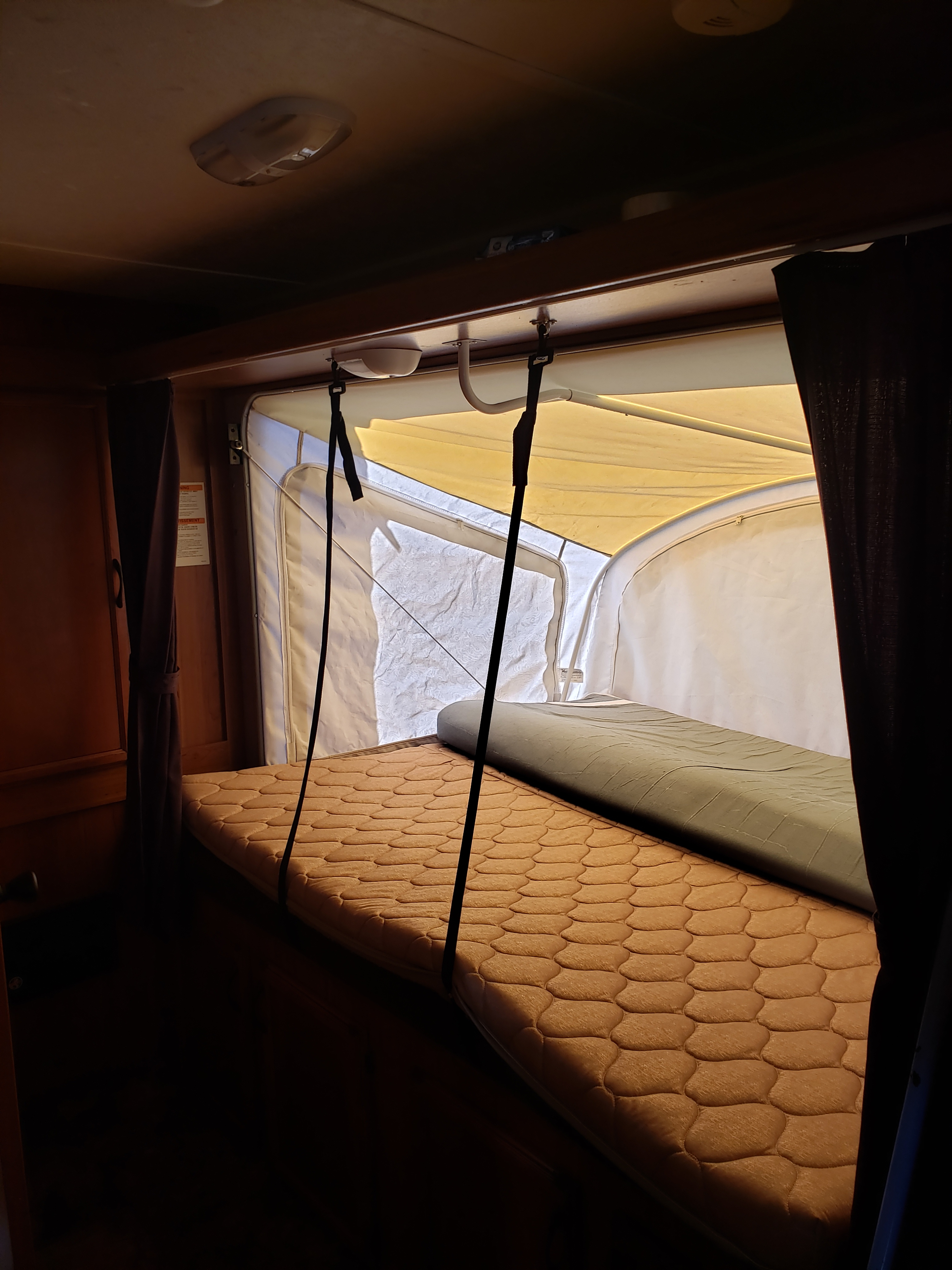 Inside an RV rental: a bright pop-out bunk features two quilted mattresses and hanging support straps. Cozy camper sleeping area.. Starcraft Launch 2015