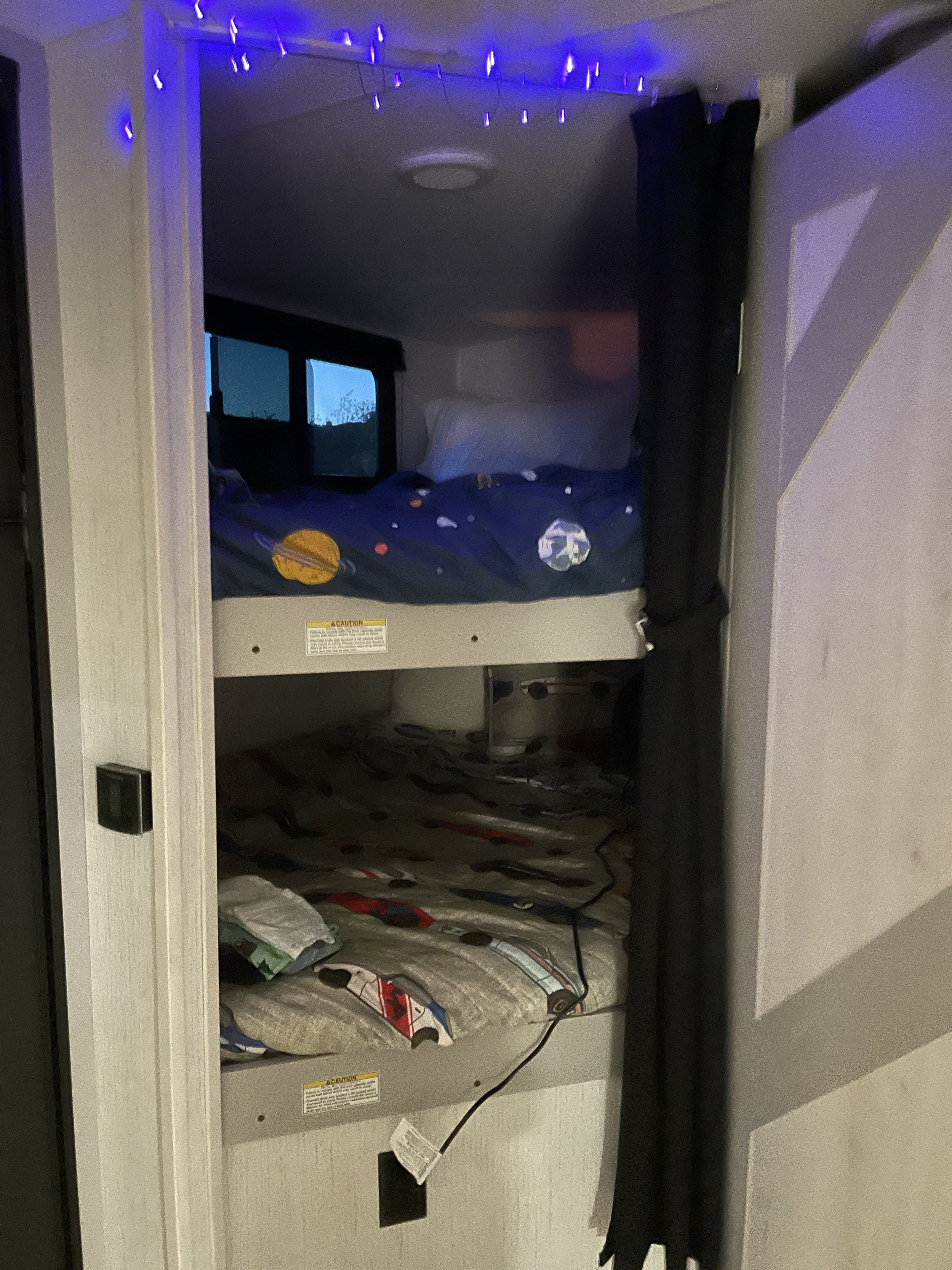 Cozy RV rental bunk beds, featuring a space-themed top bunk with a window and a lower bunk, illuminated by blue string lights.. Heartland North Trail 24BHS 2022