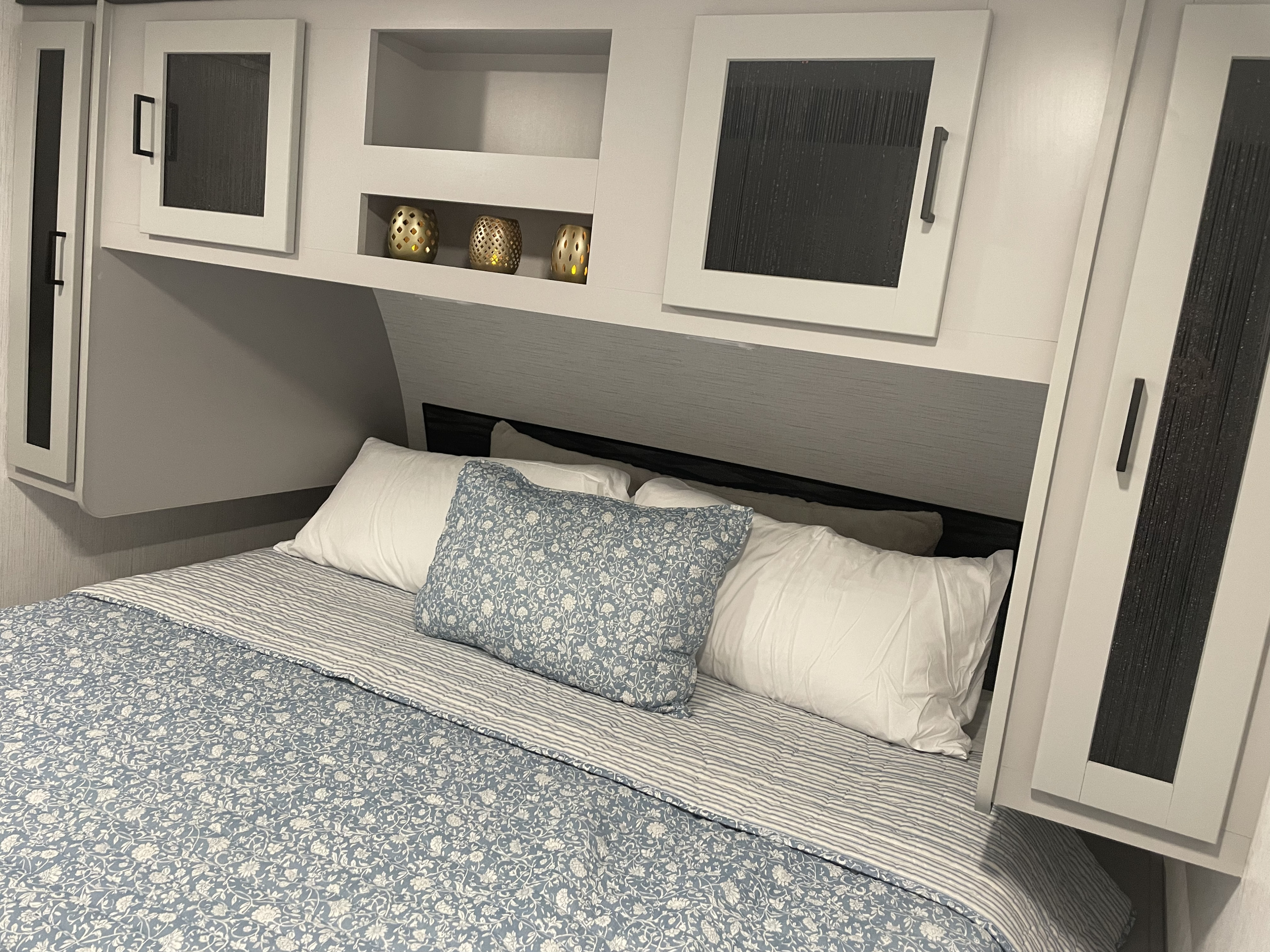 Cozy RV rental bedroom with blue and white patterned bedding, white overhead cabinets, and decorative items. Ideal for restful sleep.. Heartland North Trail 24BHS 2022