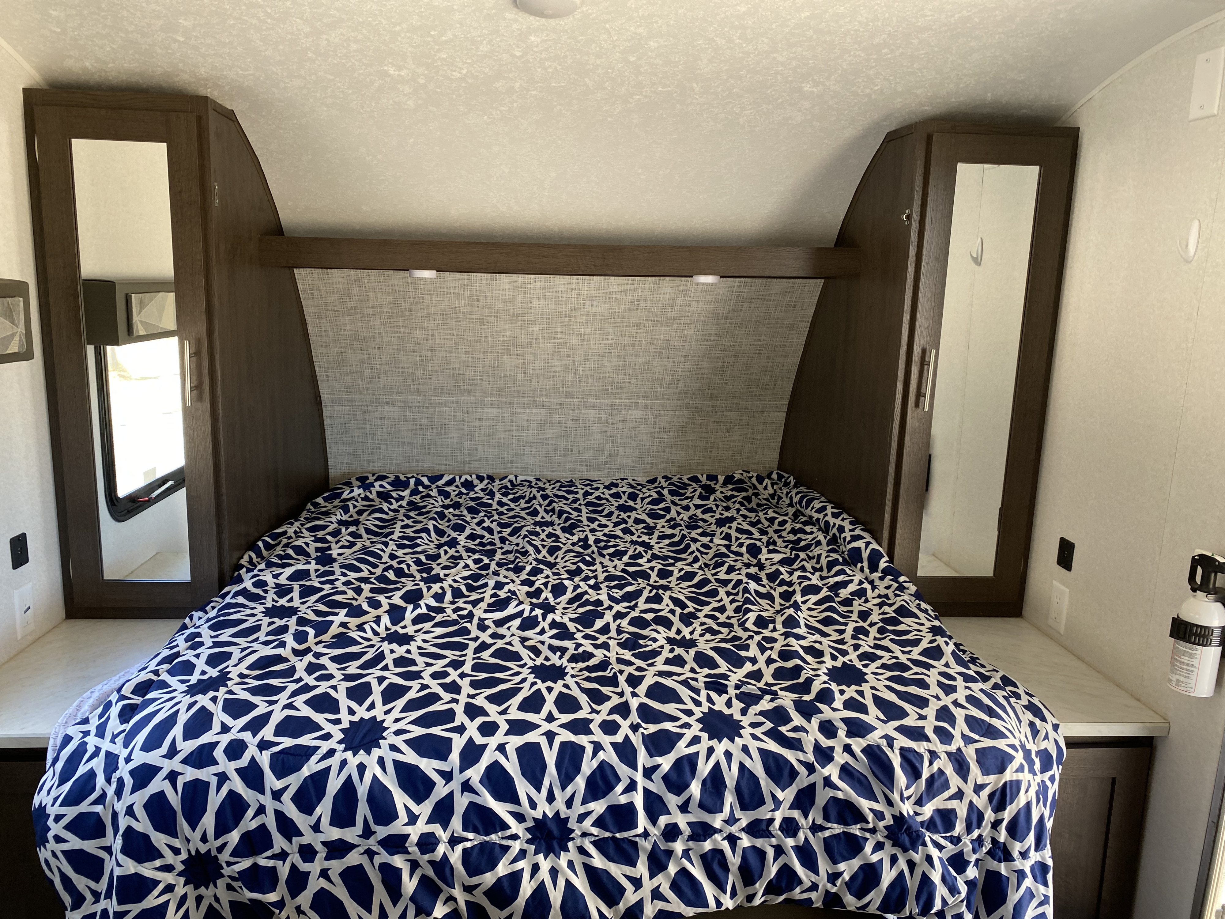 Cozy RV rental bedroom interior with blue and white bedspread, built-in storage, and wall-mounted fire extinguisher.. Forest River Wildwood X-Lite 2019