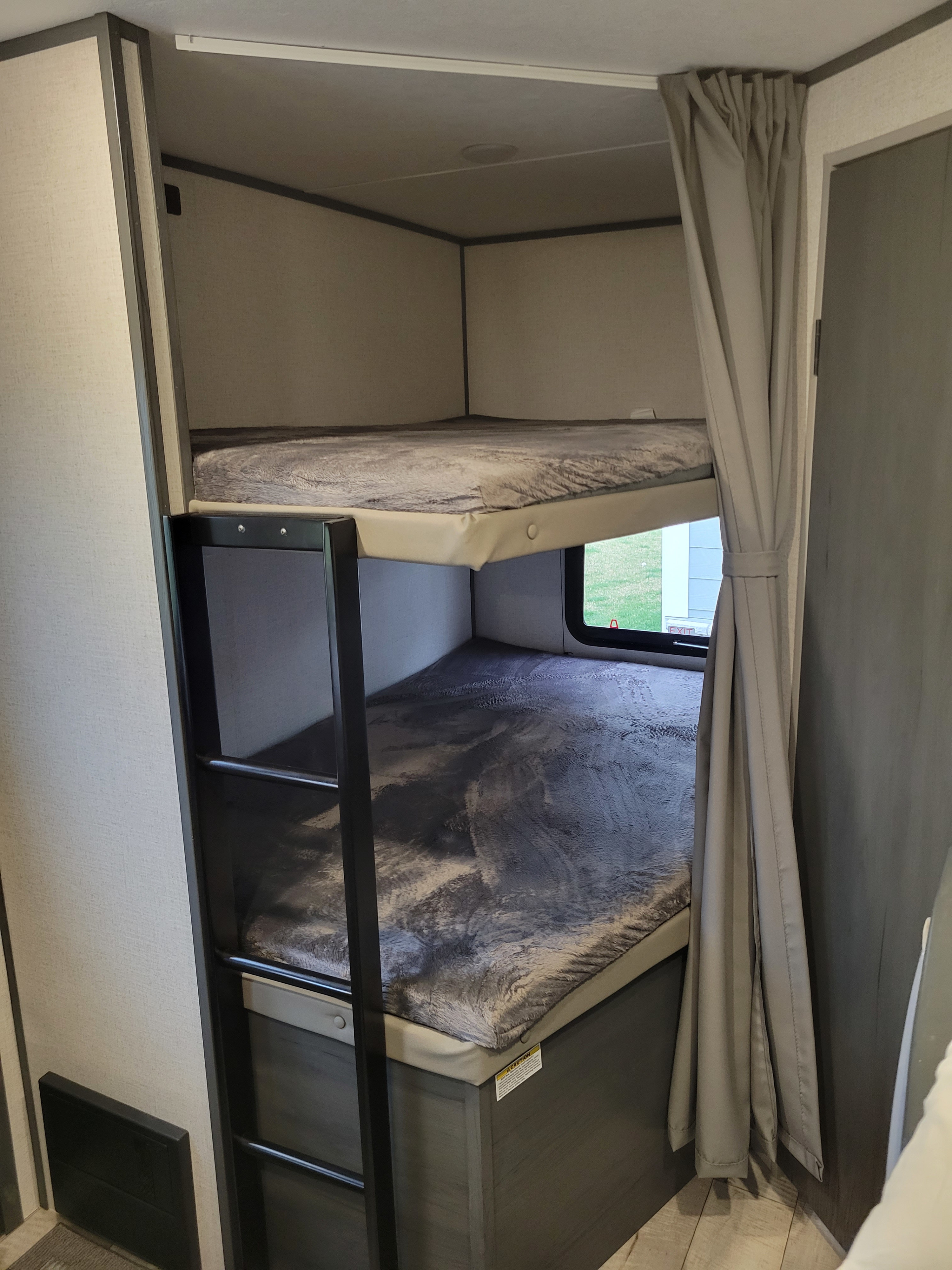 Cozy bunk beds inside an RV rental, featuring a ladder, fuzzy blankets, and a window view with an exit sign.. Dutchmen Other 2022