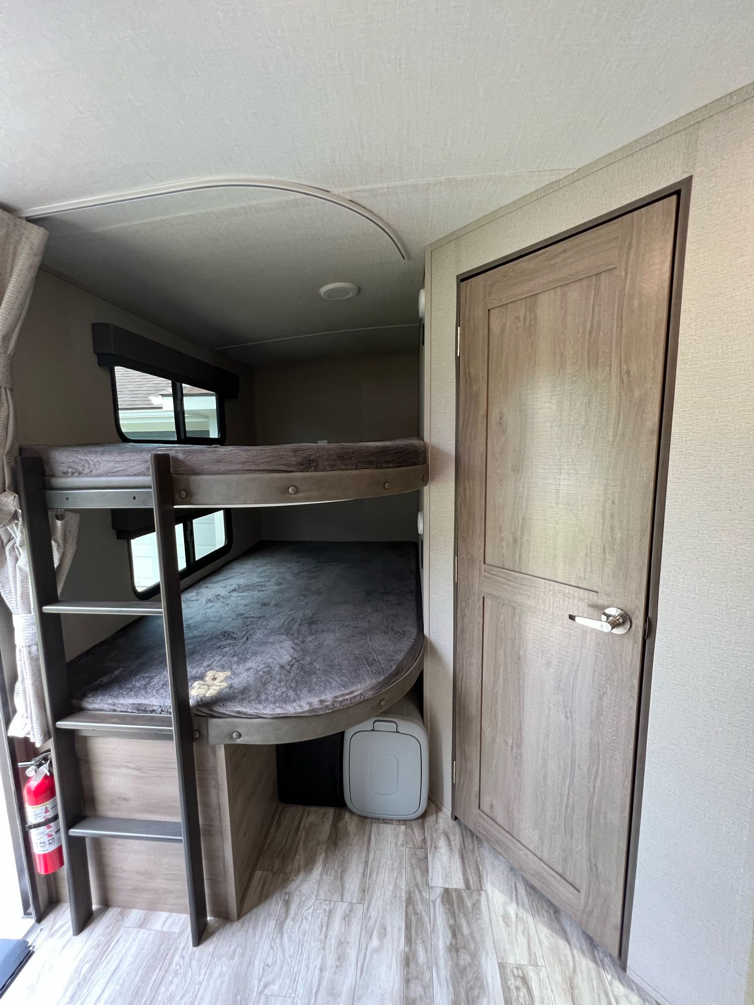 View inside an RV rental showing stacked bunk beds with windows, a ladder, and a wooden door.. Grand Design Imagine 2022