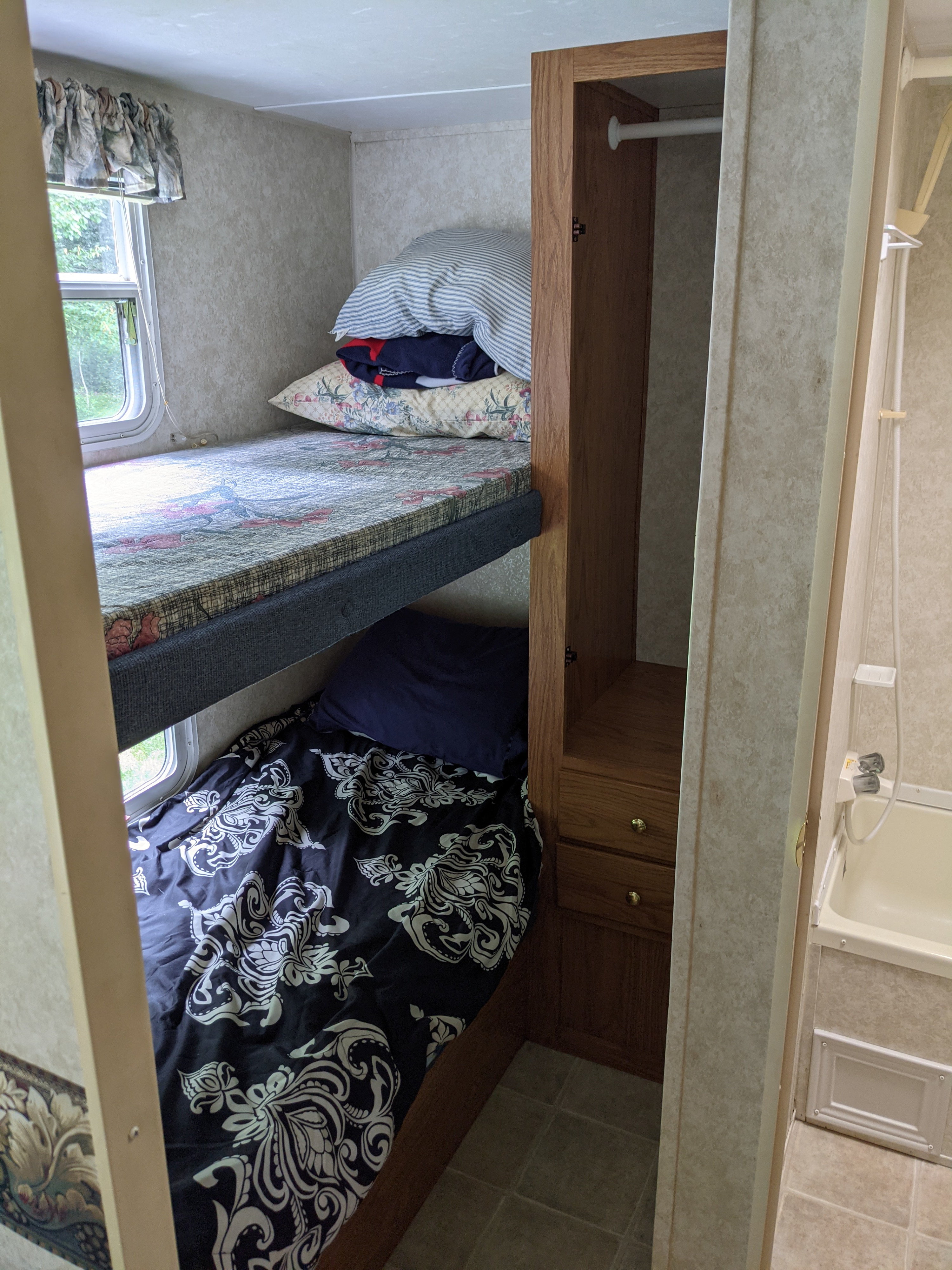 An RV rental interior with comfortable bunk beds, a handy wardrobe, and an adjacent compact bathroom.. Keystone RV Springdale 2003