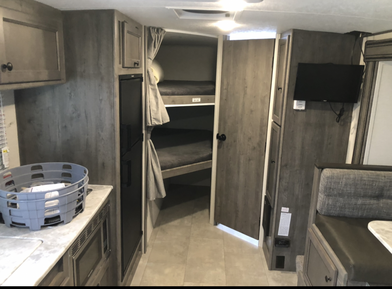 RV rental interior: cozy bunk beds, a compact kitchen with a microwave, and a comfortable dinette await your adventure.. Forest River apex 2020