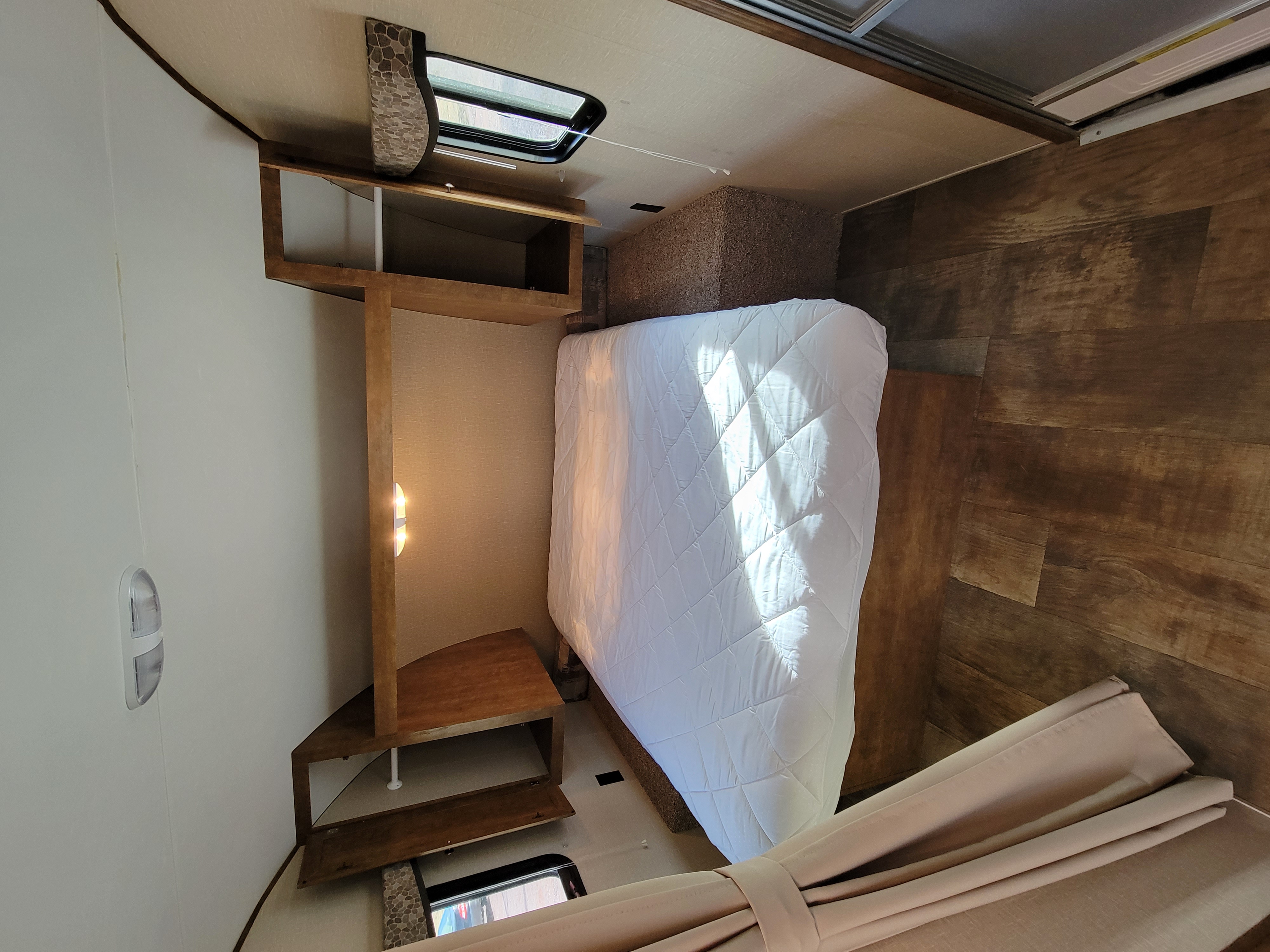RV rental bedroom featuring a clean, white-covered bed, wooden shelving, and wood plank flooring, ready for guests.. Crossroads RV Z-1 2015